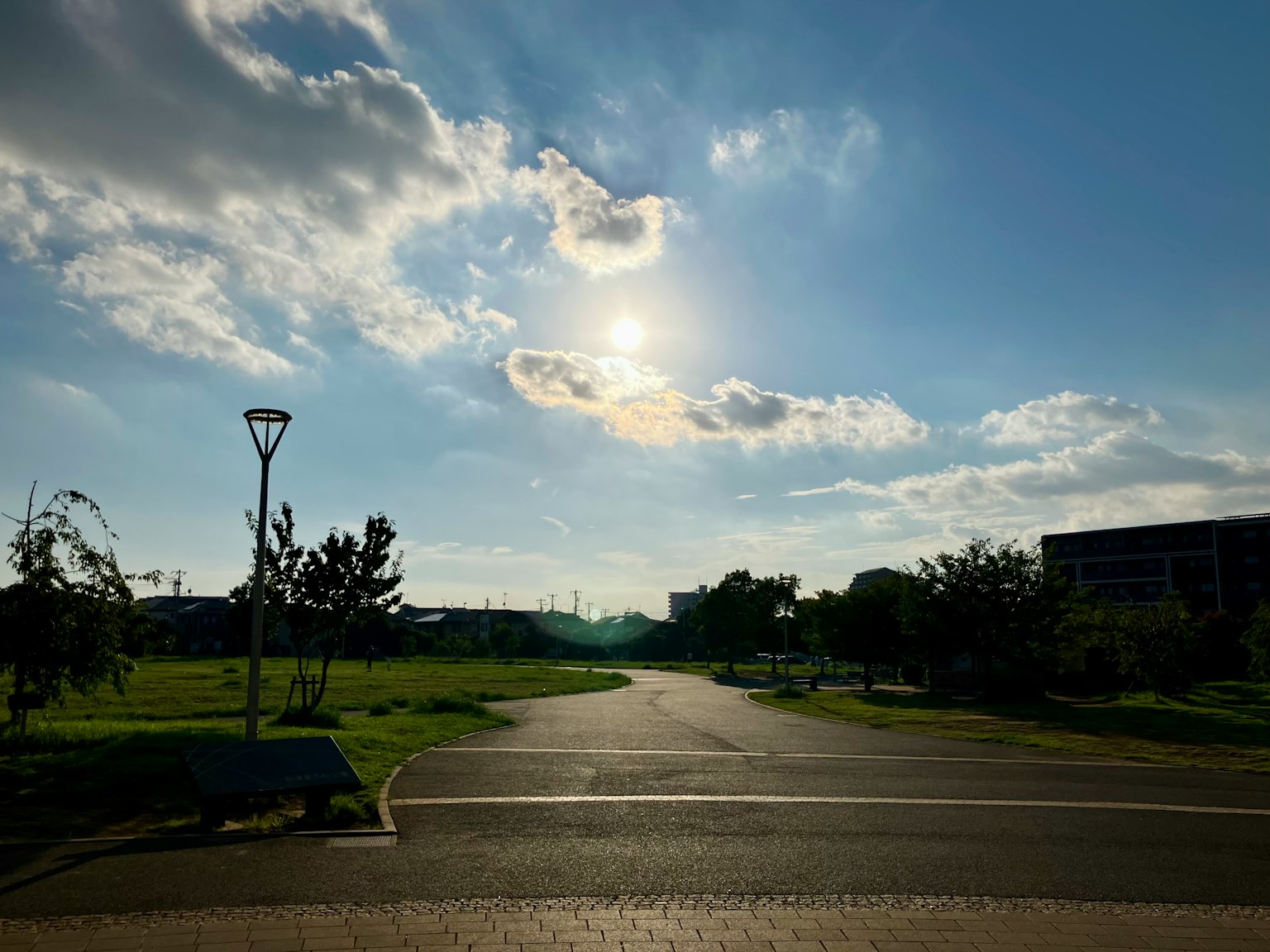 Parkszene mit blauem Himmel und strahlender Sonne mit einer Straße und grünem Gras