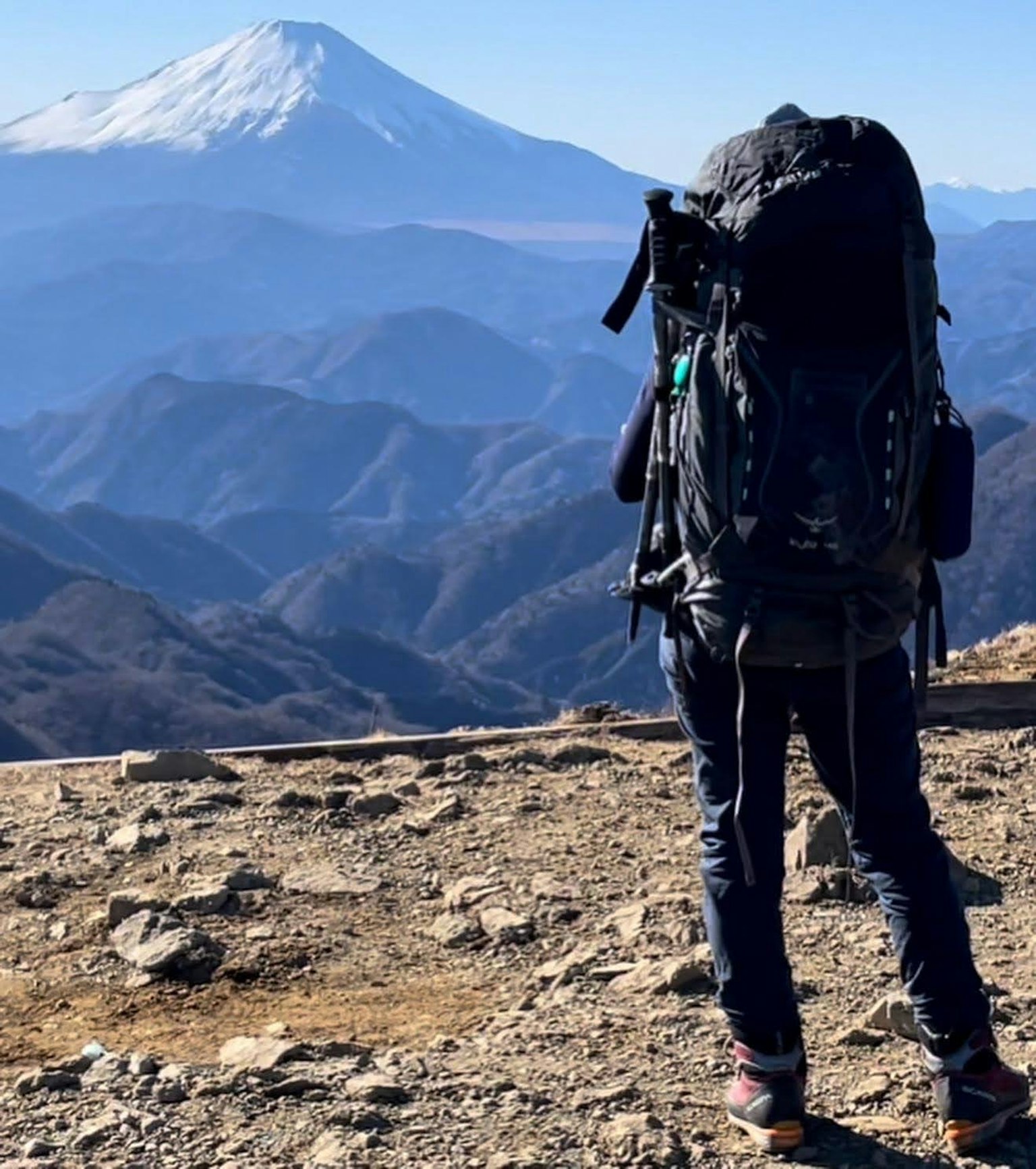 Wanderer mit einem großen Rucksack, der auf einen verschneiten Berg in der Ferne blickt