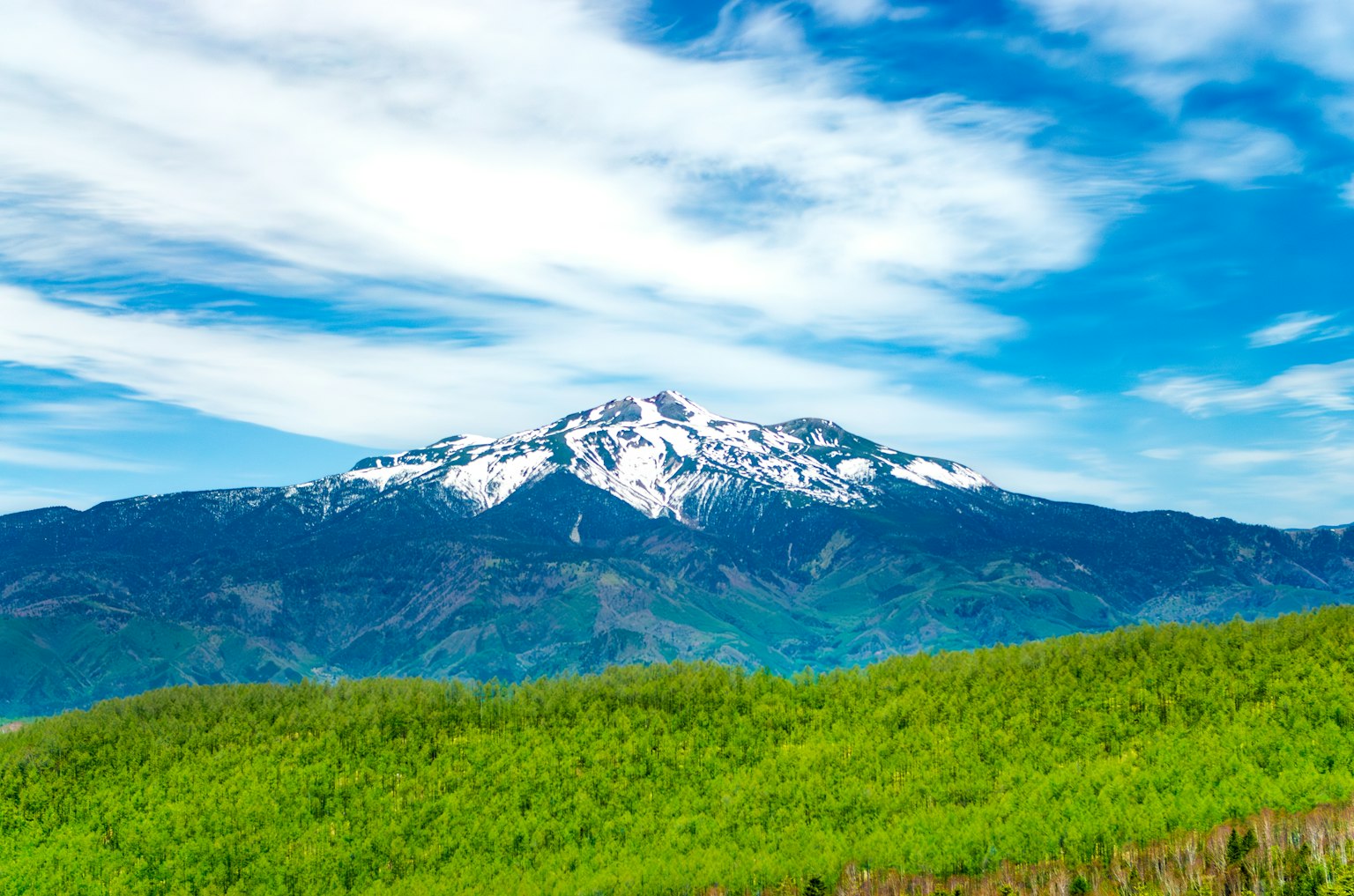 Mont enneigé sous un ciel bleu avec des collines vertes