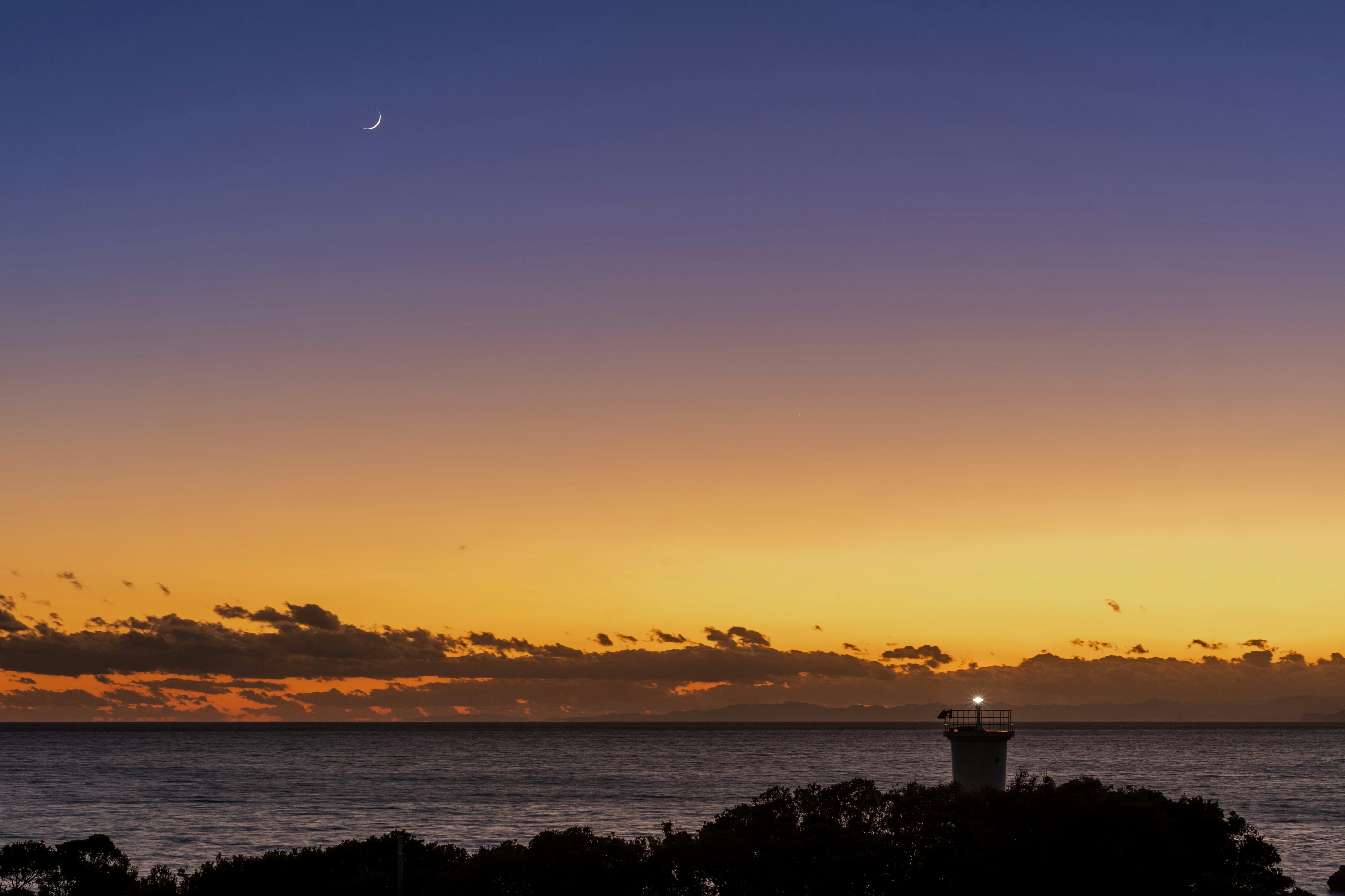 夕焼けの海と灯台のある海岸の風景