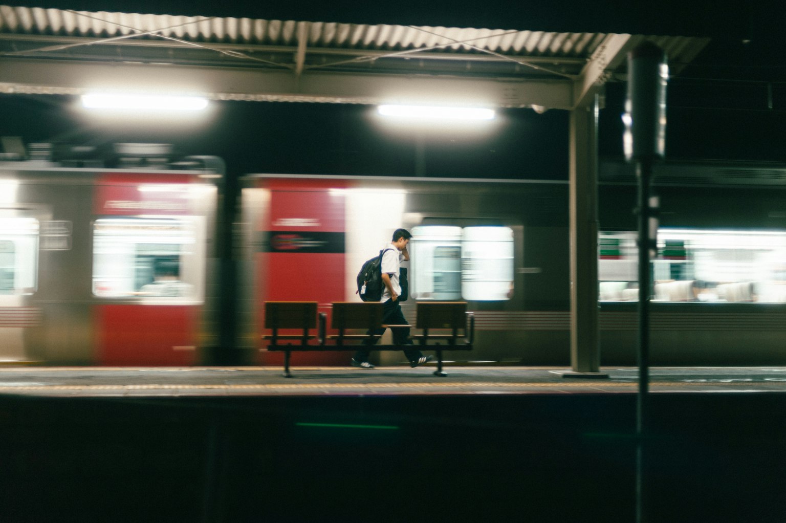 Eine Person sitzt auf einer Bank an einem Bahnhof, während ein Zug nachts vorbeifährt
