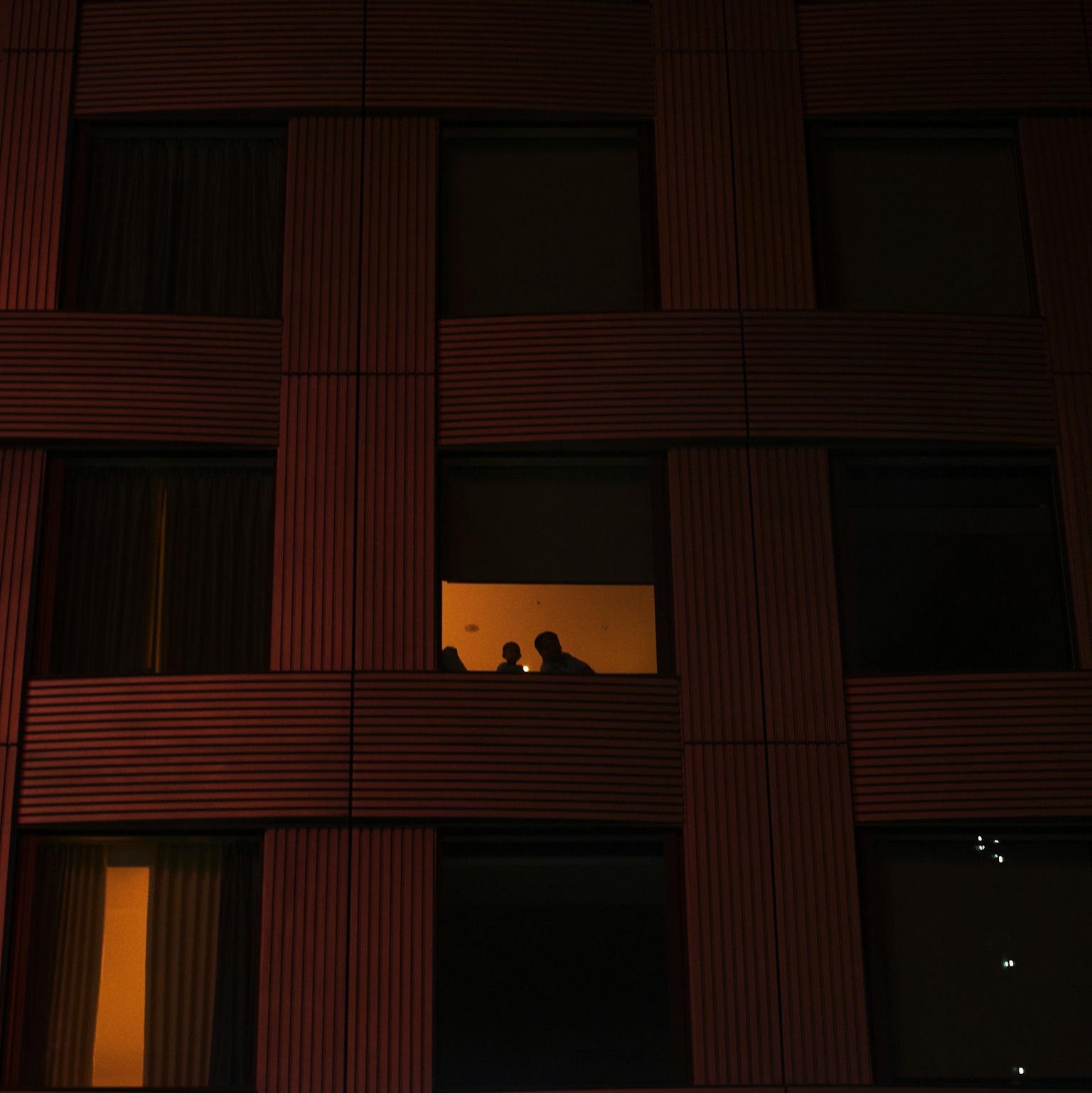 Silhouettes of two people visible through a window at night with warm light