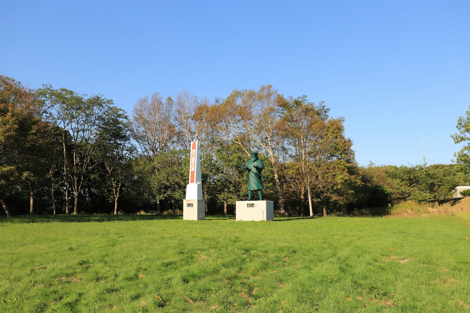 Zwei Statuen stehen auf einer grünen Wiese unter einem blauen Himmel mit Bäumen im Hintergrund
