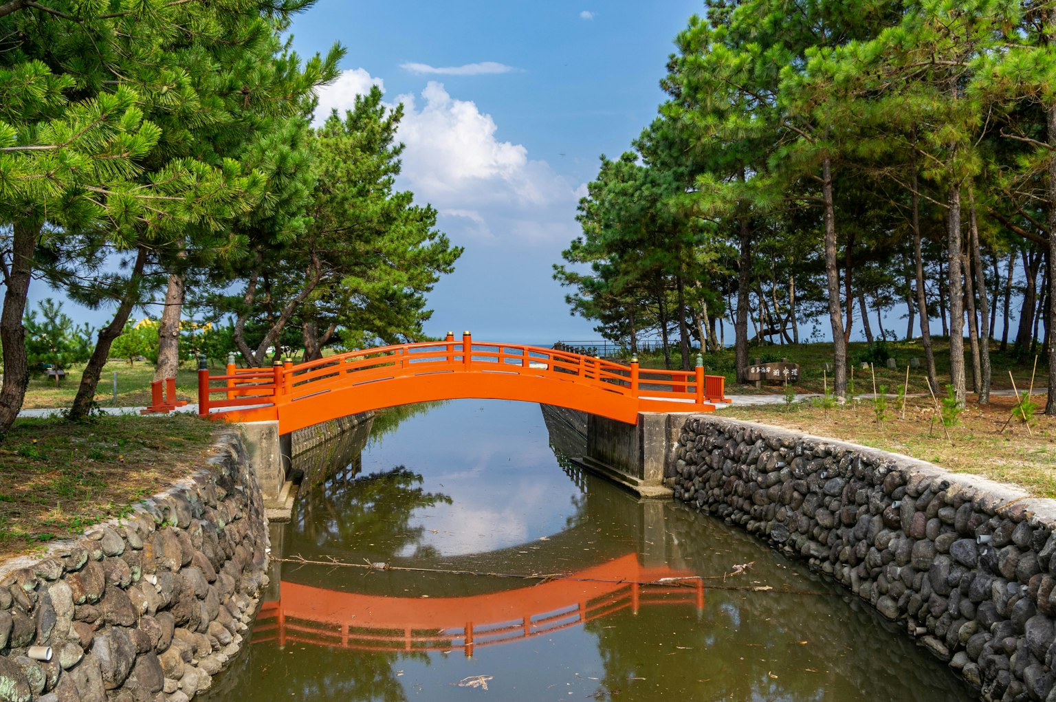 ทิวทัศน์ที่สวยงามของสวนสีเขียวสดใสพร้อมสะพานสีส้มสะท้อนในน้ำ