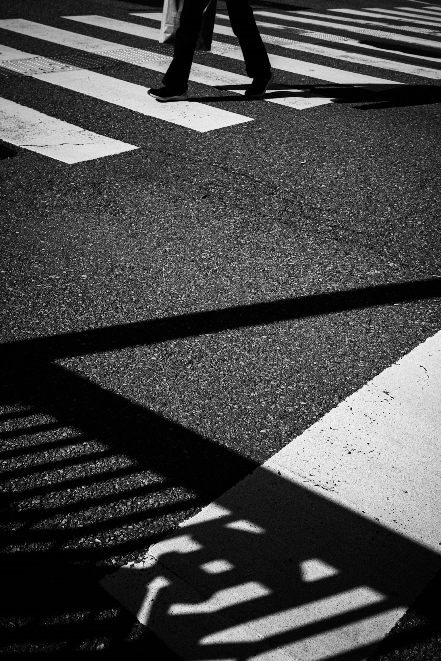 Silhouette di una persona che cammina su un attraversamento pedonale in bianco e nero con forte contrasto di ombre
