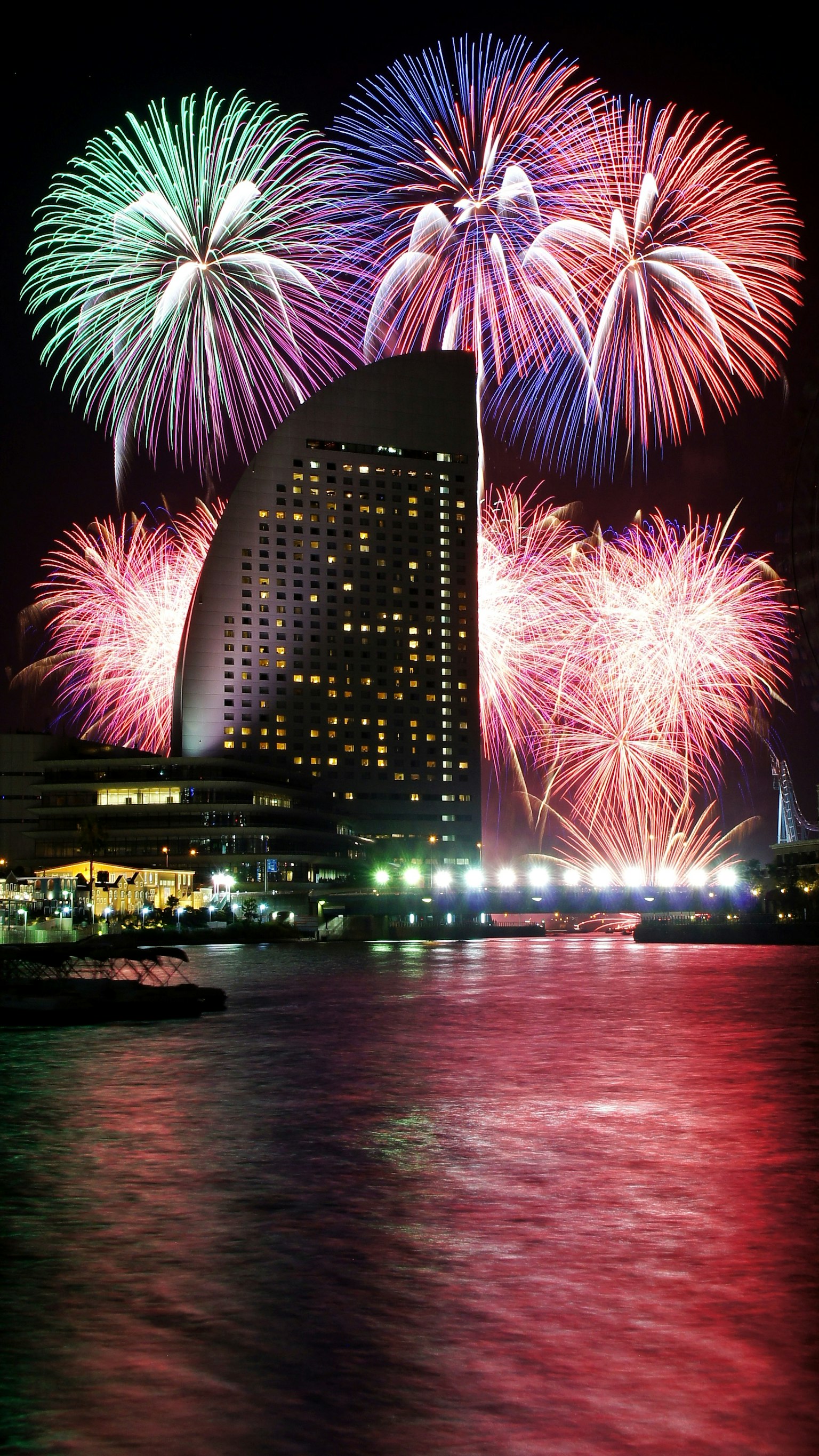 Fuochi d'artificio colorati illuminano il cielo notturno con un famoso punto di riferimento di Yokohama che si riflette nell'acqua