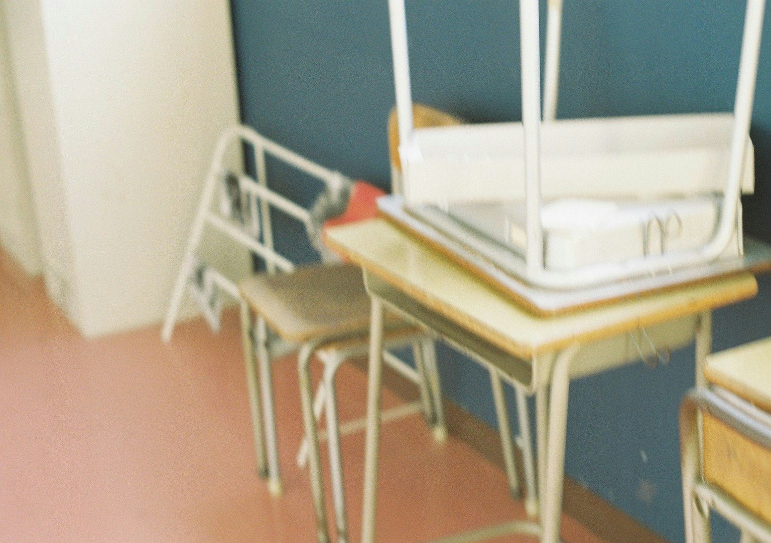 Klassenzimmerszene mit gestapelten Stühlen und Tischen vor einer blauen Wand und einem rosa Boden