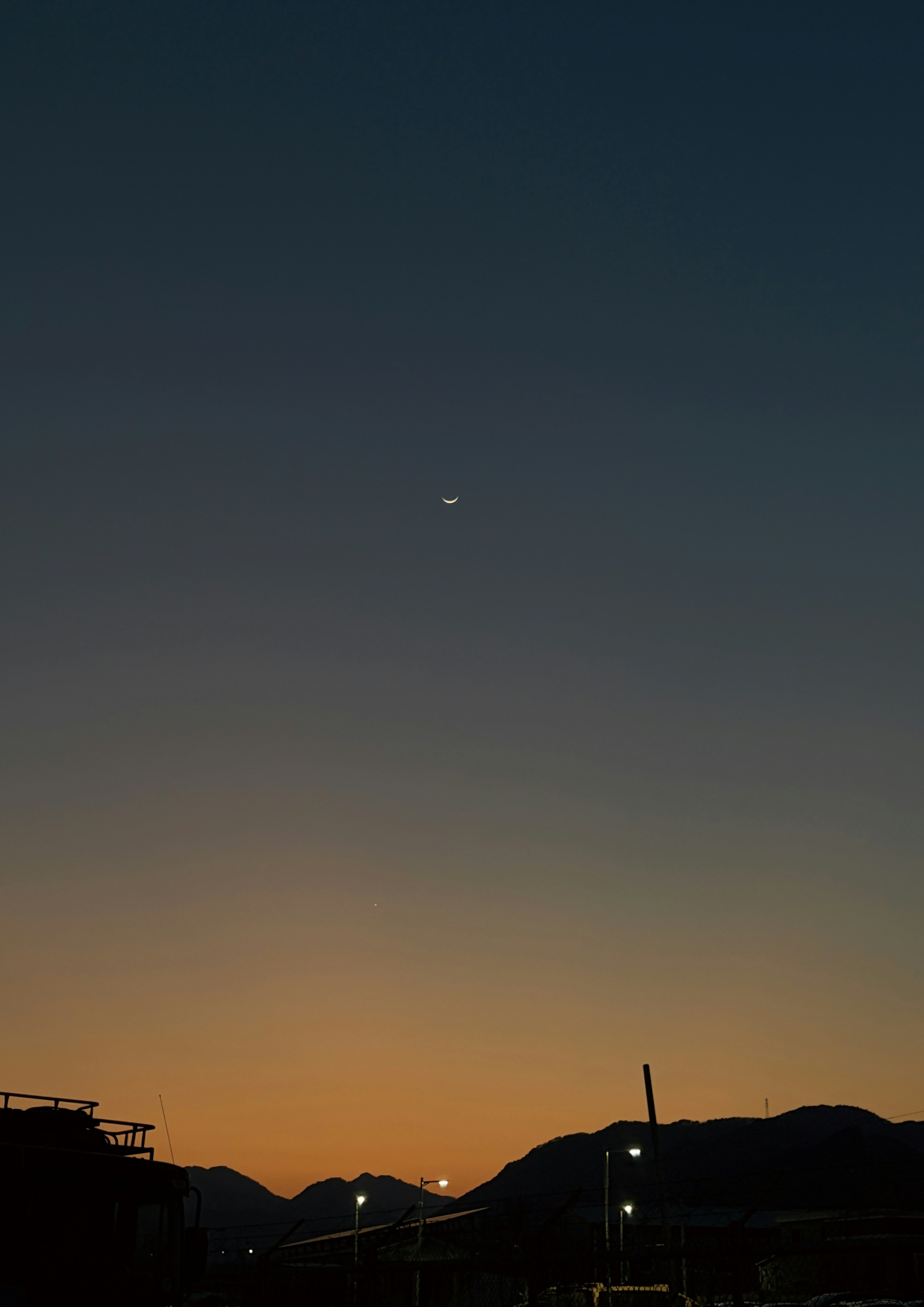 夕暮れの空に浮かぶ月と山並みのシルエット