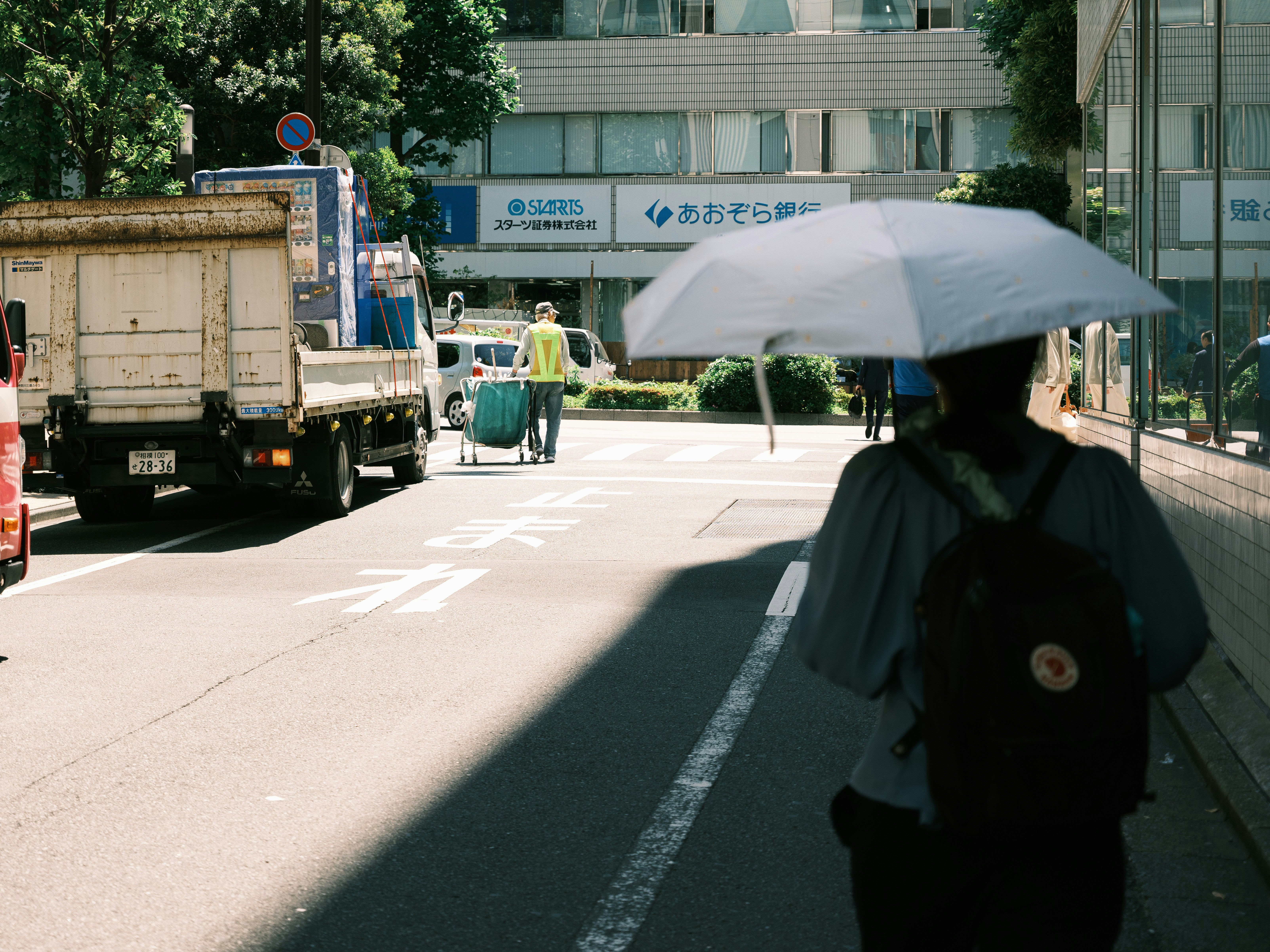路口行人撐傘與卡車通過的街景
