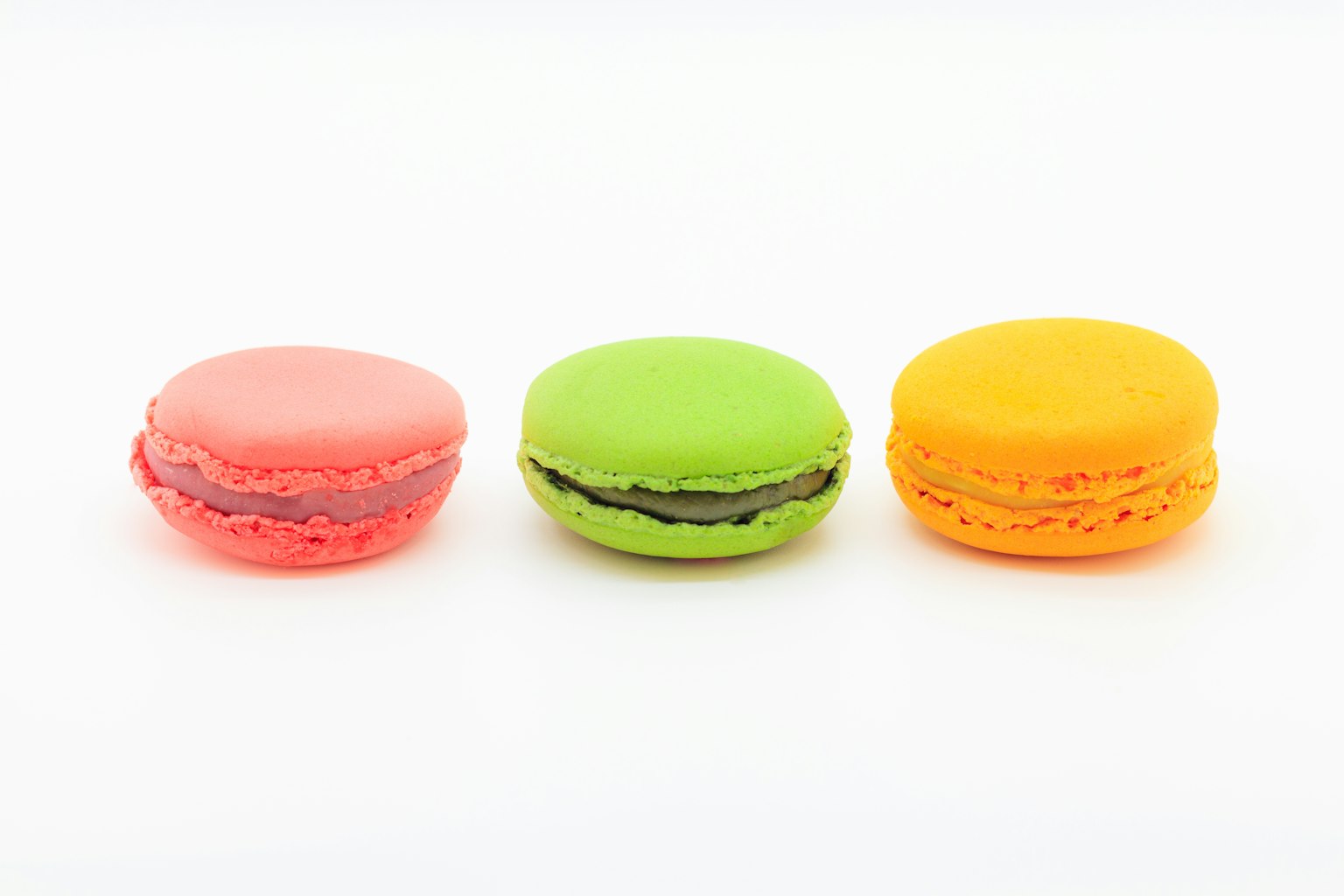 Three colorful macarons in pink, green, and orange arranged on a white background