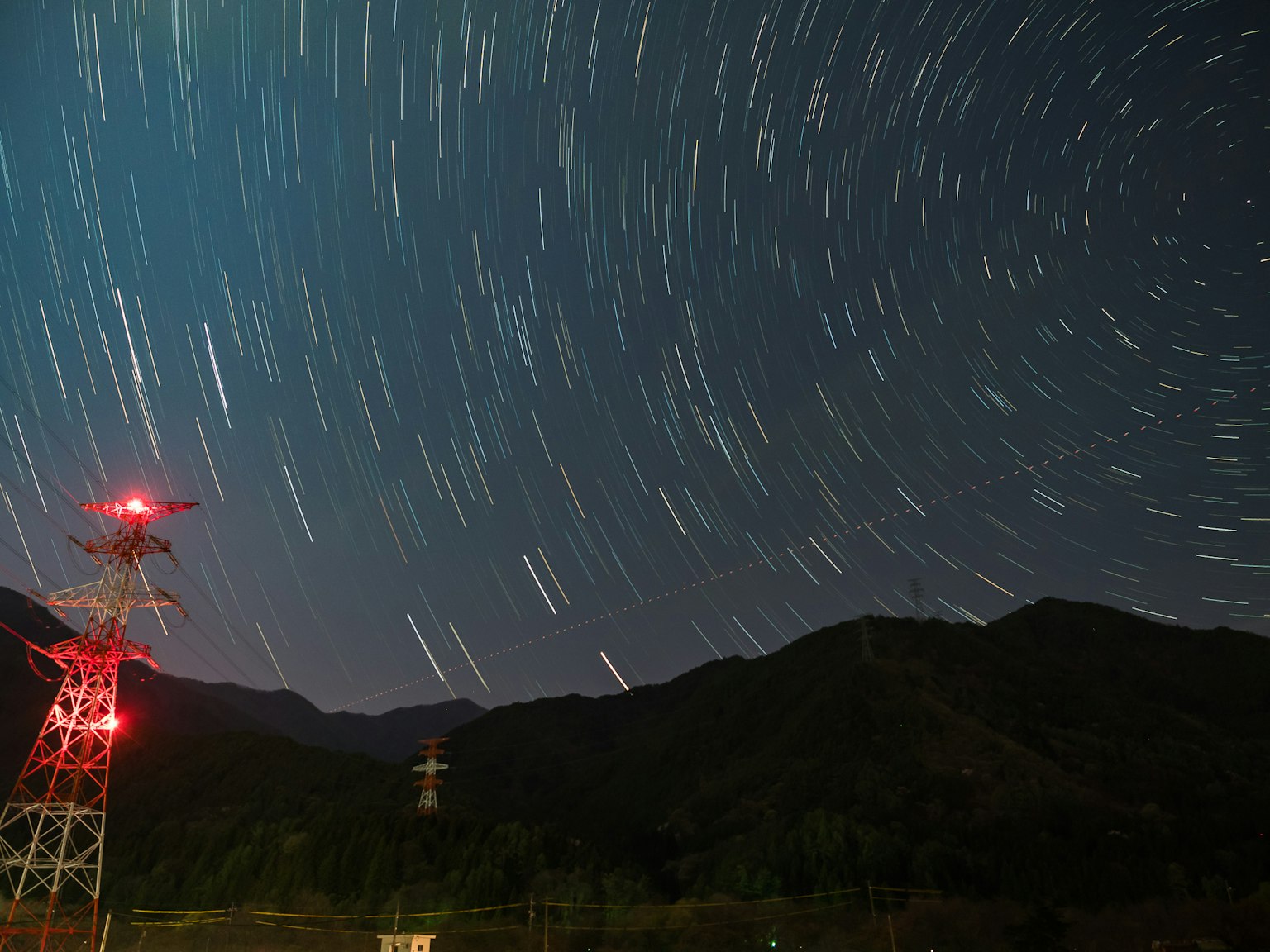 Ciel nocturne avec des traînées d'étoiles et un pylône électrique avec des lumières rouges