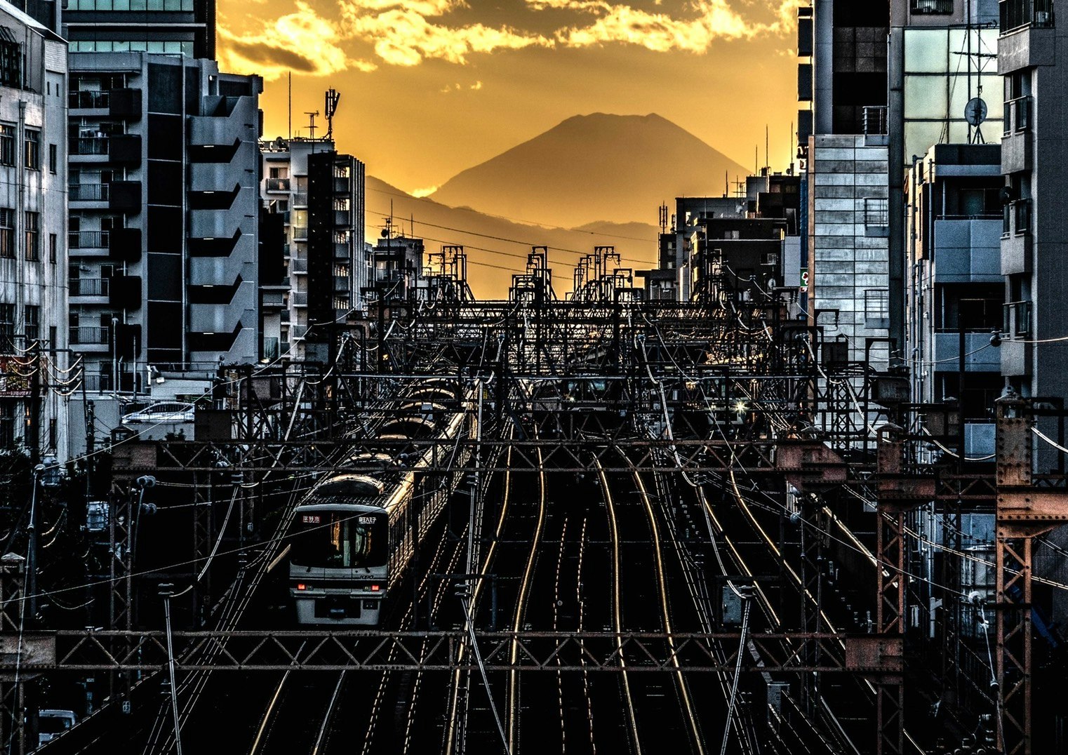 夕日を背景にした富士山と鉄道の風景 高層ビルと電線が交差する都市の景観