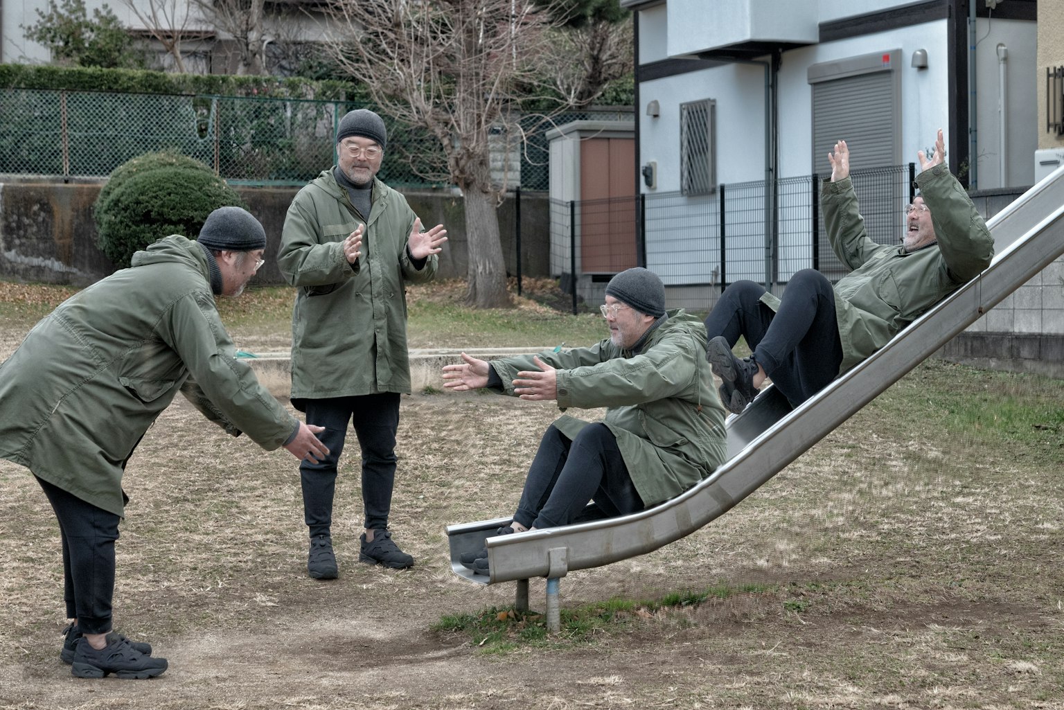 People playing on a slide in a park Four individuals in green coats
