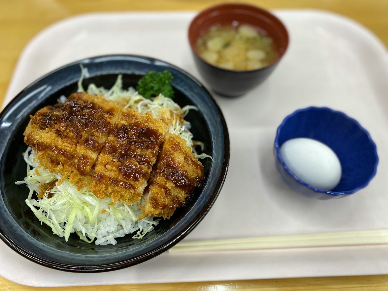 Plato de tonkatsu servido sobre repollo rallado con sopa de miso y un huevo pasado por agua al lado