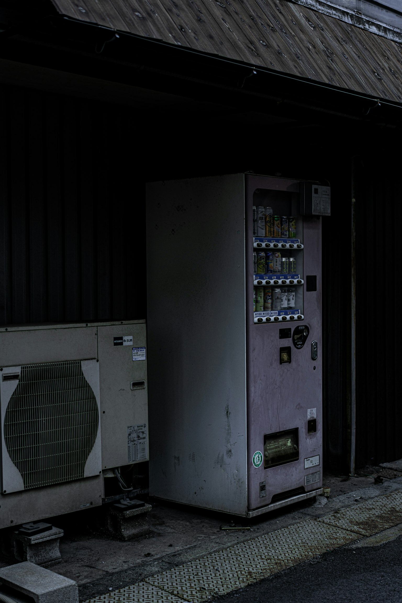 古い自動販売機とエアコンが並ぶ暗い路地の風景