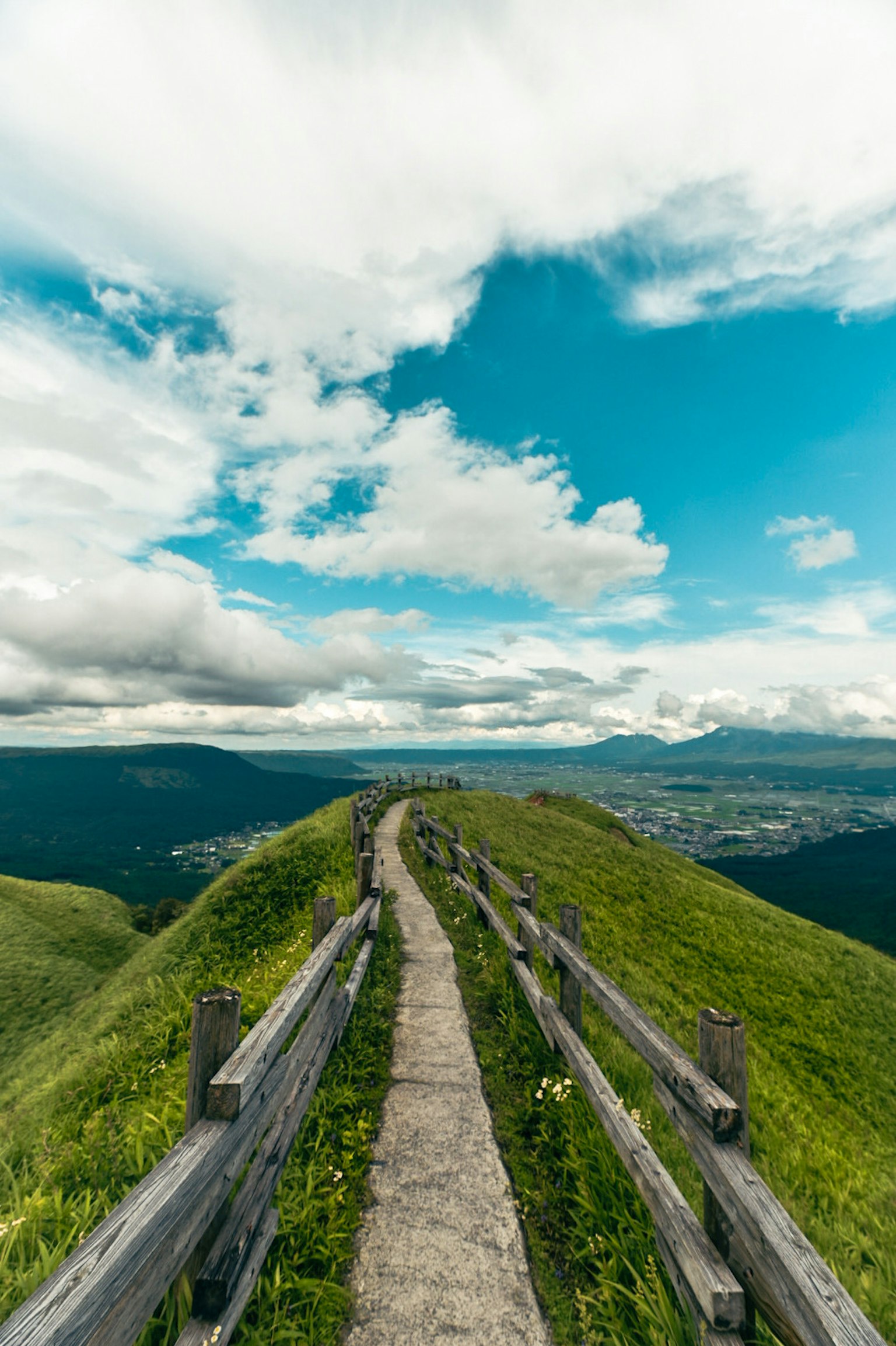 Chemin pavé sur une colline verte avec une clôture en bois sous un ciel bleu avec des nuages blancs