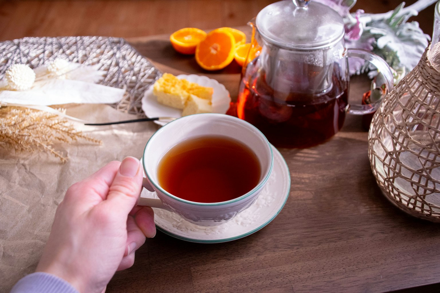 手握黑茶杯，旁边有茶壶和橙子、黄油