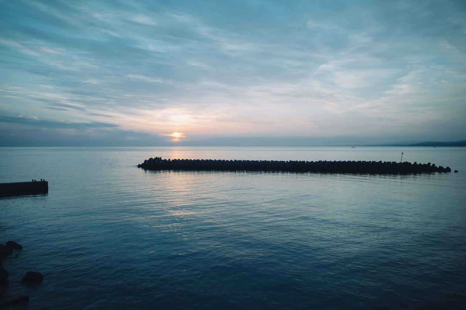 Ruhiges Meer mit sichtbarem Sonnenuntergang Dunkle Wasseroberfläche und bewölkter Himmel