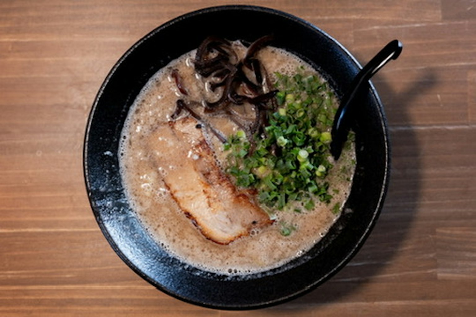Sup ramen dalam mangkuk hitam dengan irisan daging babi dan bawang hijau