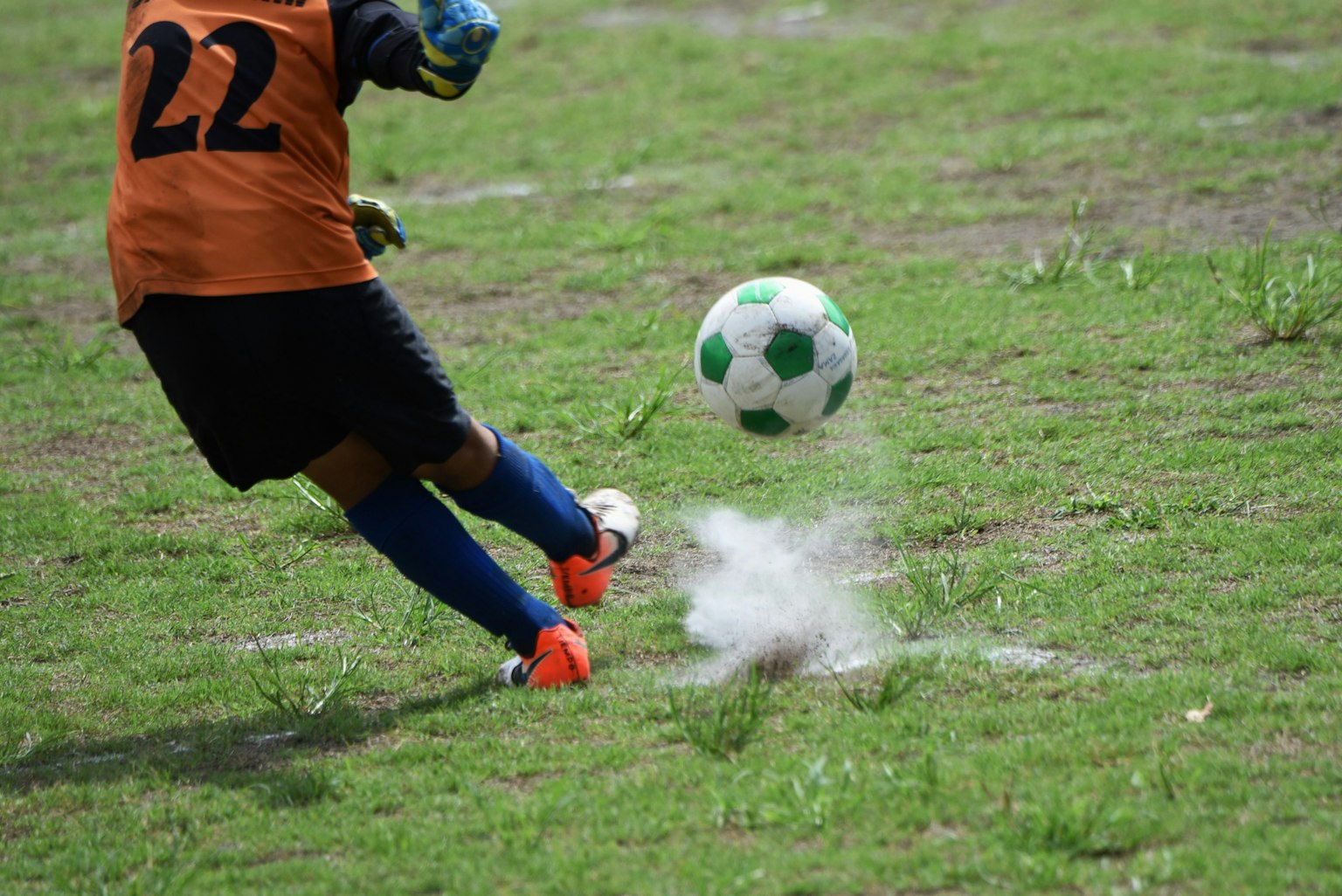 Joueur de football frappant un ballon en mouvement portant un maillot orange avec le numéro 22 sur de l'herbe verte