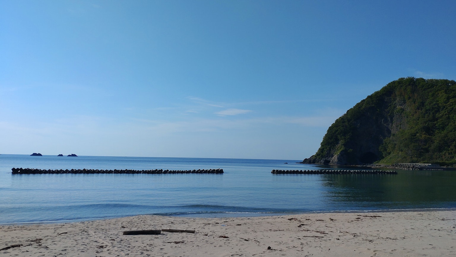 Malerei von einem blauen Meer und einem ruhigen Strand mit einem grünen Hügel im Hintergrund