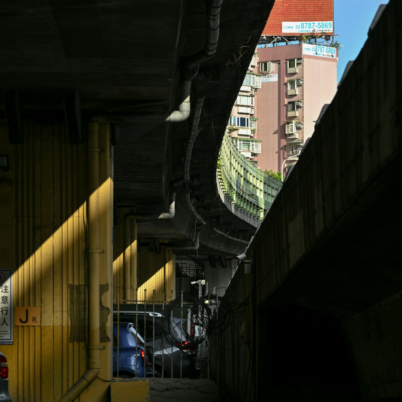 Vue d'un parking sous une route surélevée avec des murs jaunes brillants et des ombres contrastées