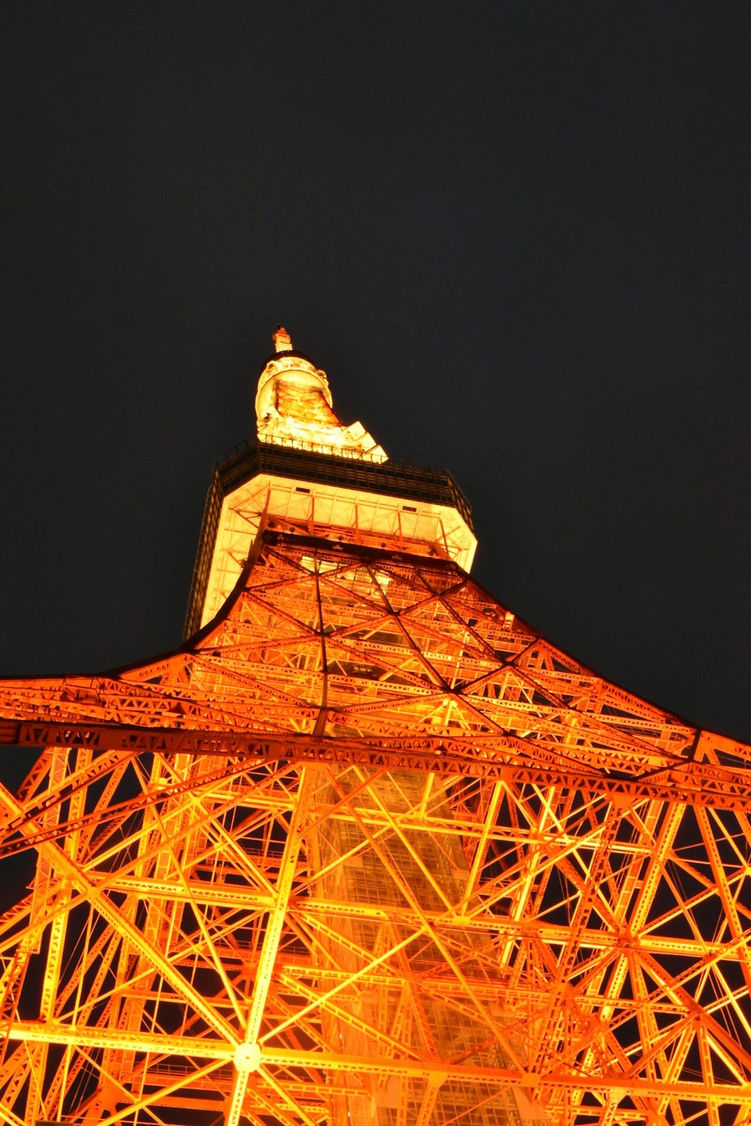 Photo de la Tour de Tokyo vue de dessous la nuit mettant en valeur sa structure orange lumineuse