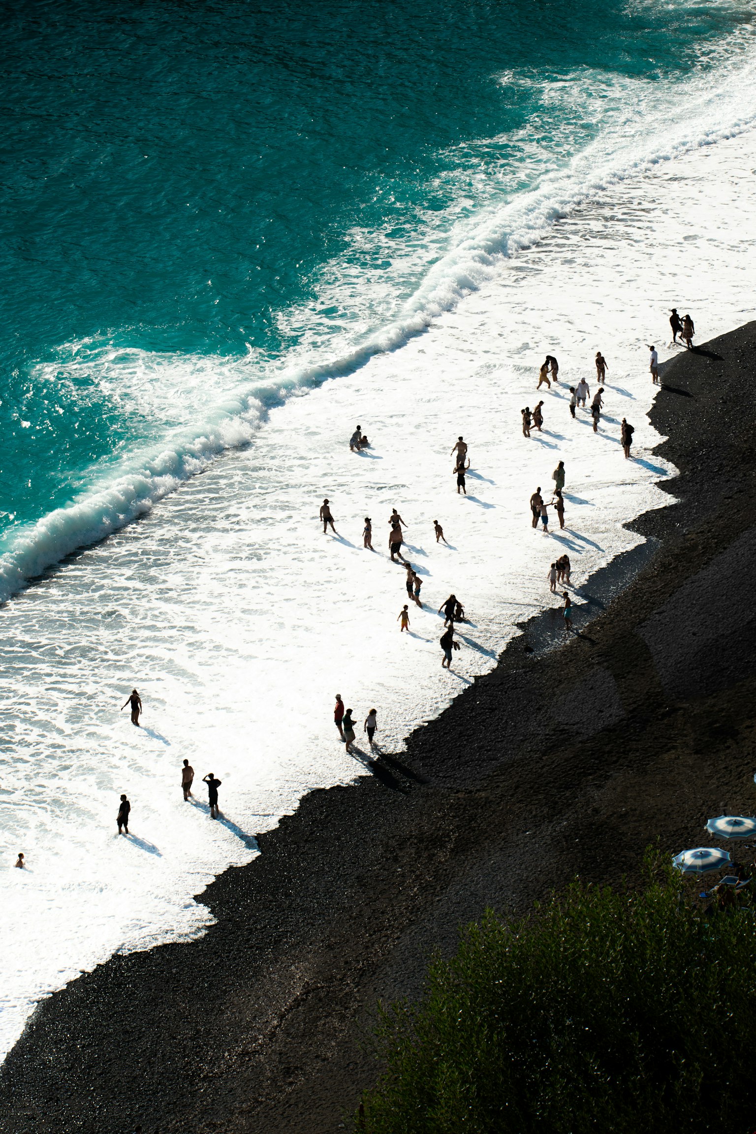 海岸で遊ぶ人々のシルエットと青い海の波