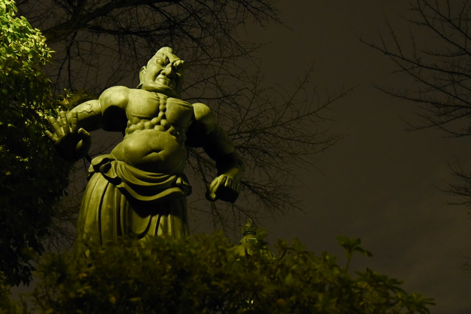 Statua gigante di divinità in piedi di notte illuminata da luce verde
