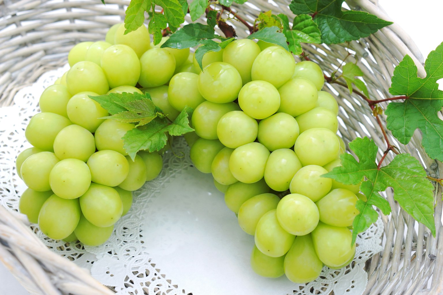 Uvas verdes frescas dispuestas en una cesta blanca con hojas decorativas