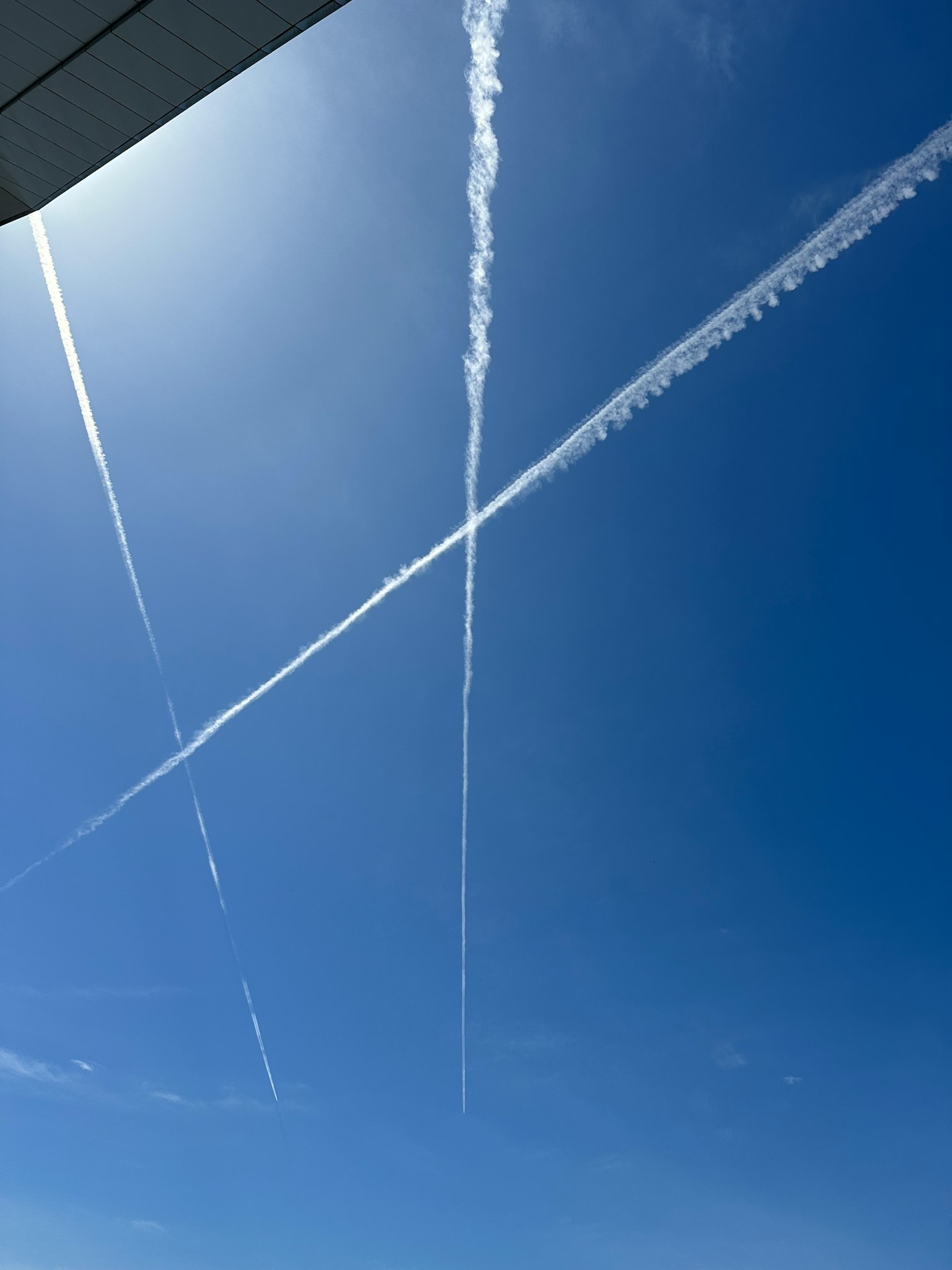 Kondensstreifen, die ein sich kreuzendes Muster im blauen Himmel bilden