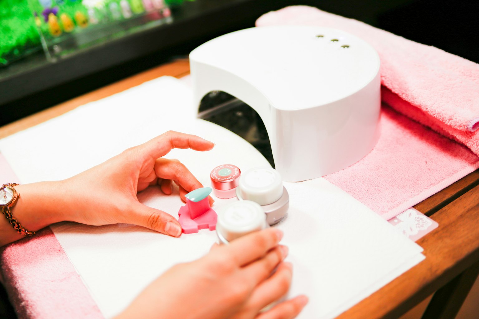 Manos aplicando esmalte de uñas con una lámpara UV en un salón de uñas
