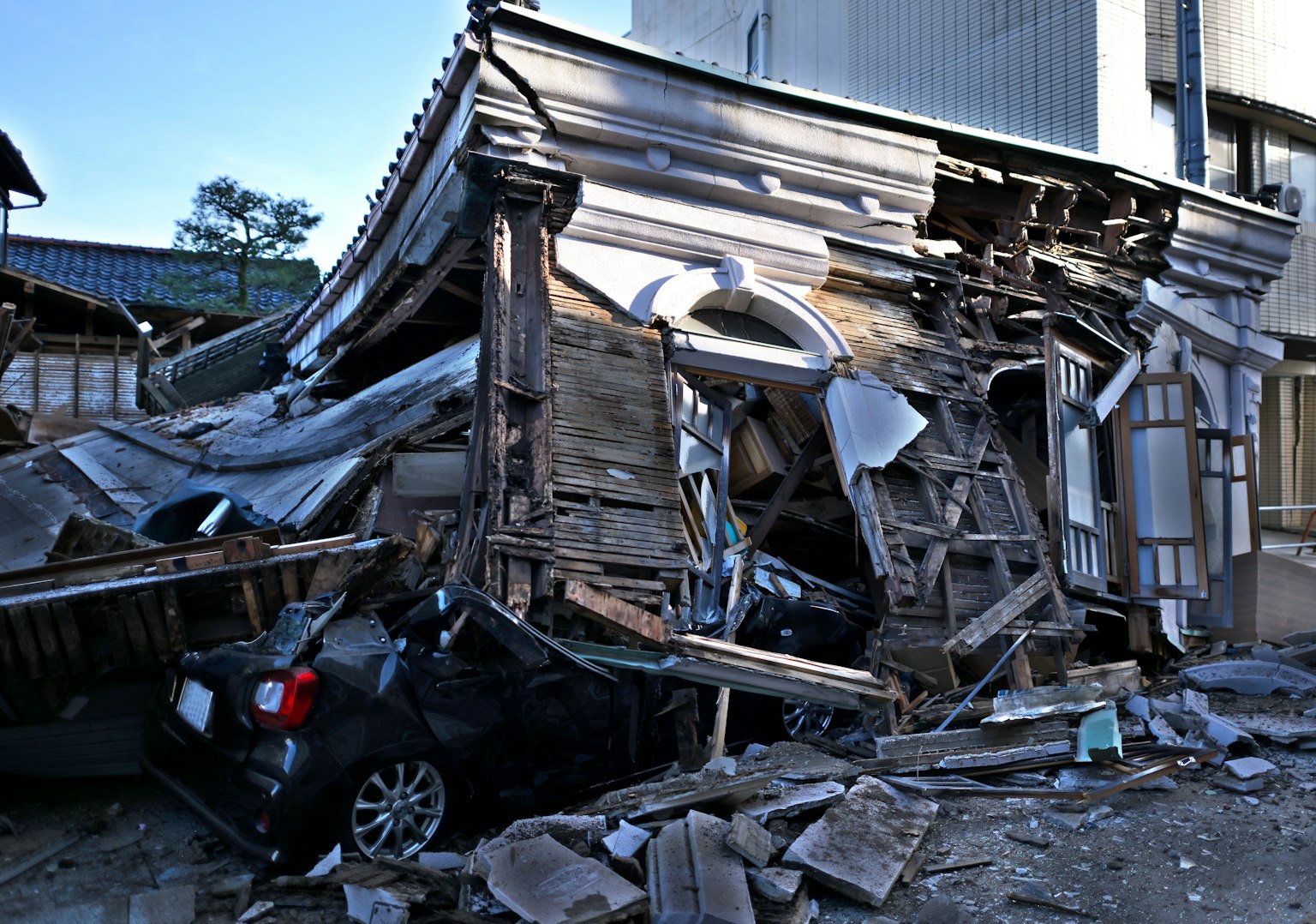 Eingestürztes traditionelles japanisches Haus mit beschädigtem Auto davor