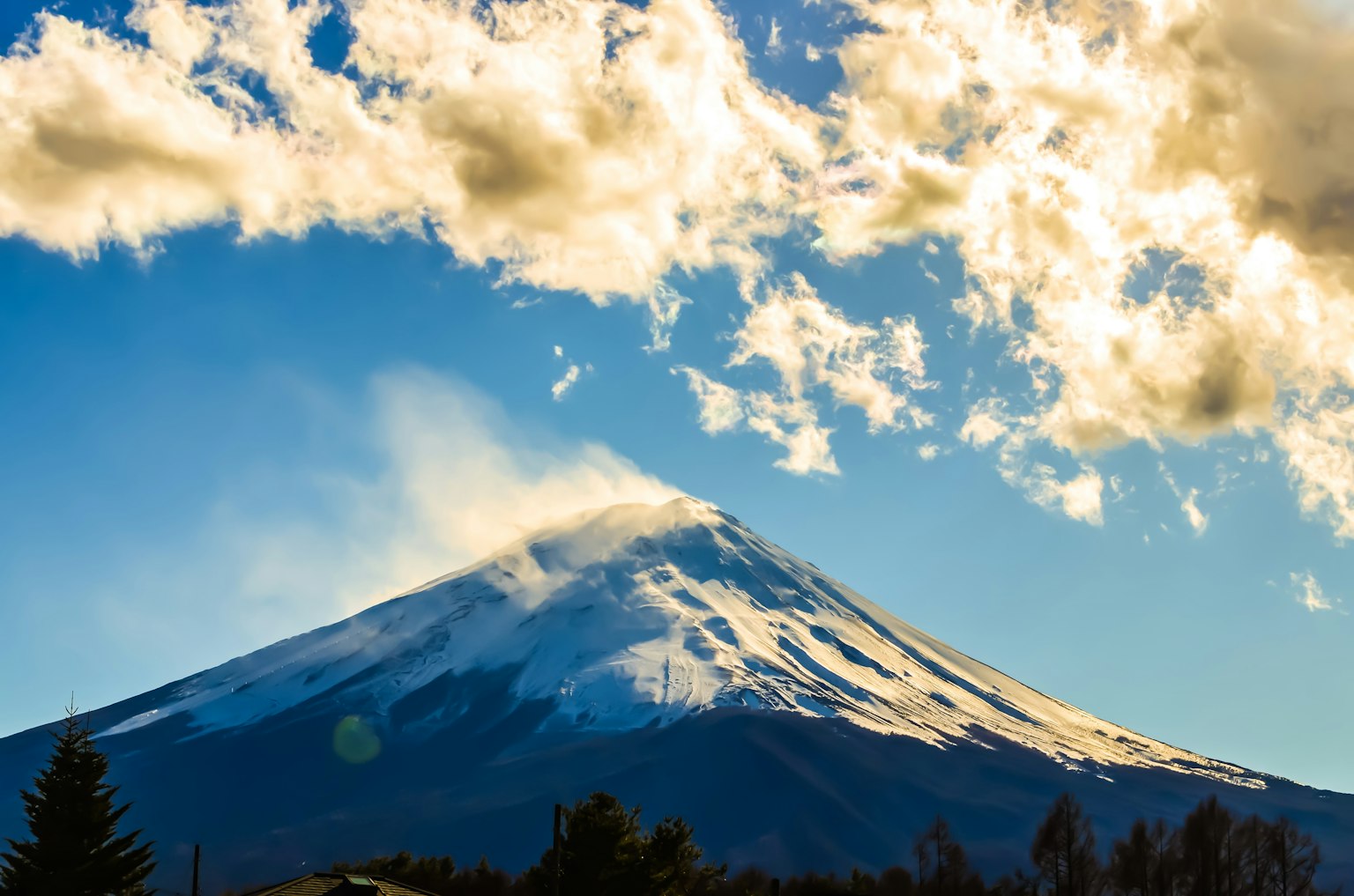 Snow-capped peak of Mount Fuji against a blue sky with clouds