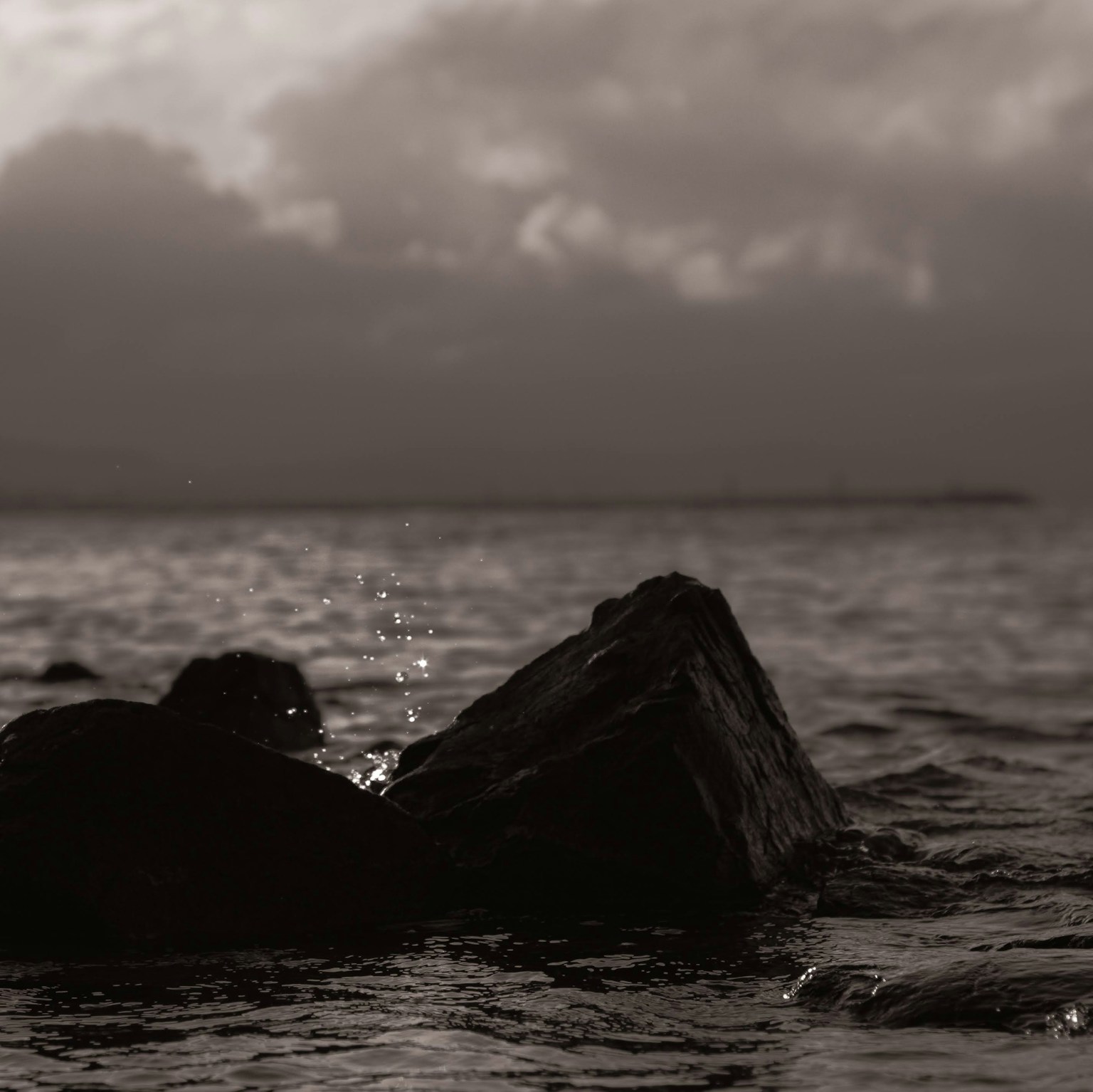 Monochrome landscape featuring rocks in the sea with splashes of water