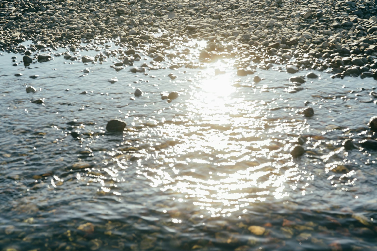 Eine Ansicht von Sonnenlicht, das sich auf Wasser spiegelt, mit sichtbaren Kieselsteinen