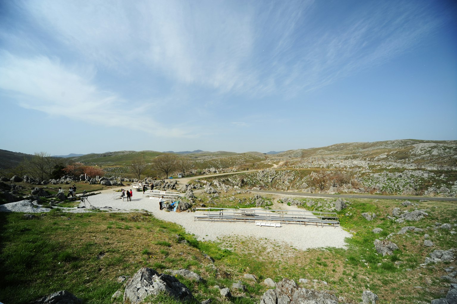 Vista panorámica de un sitio arqueológico rodeado de vegetación con visitantes bajo un cielo azul