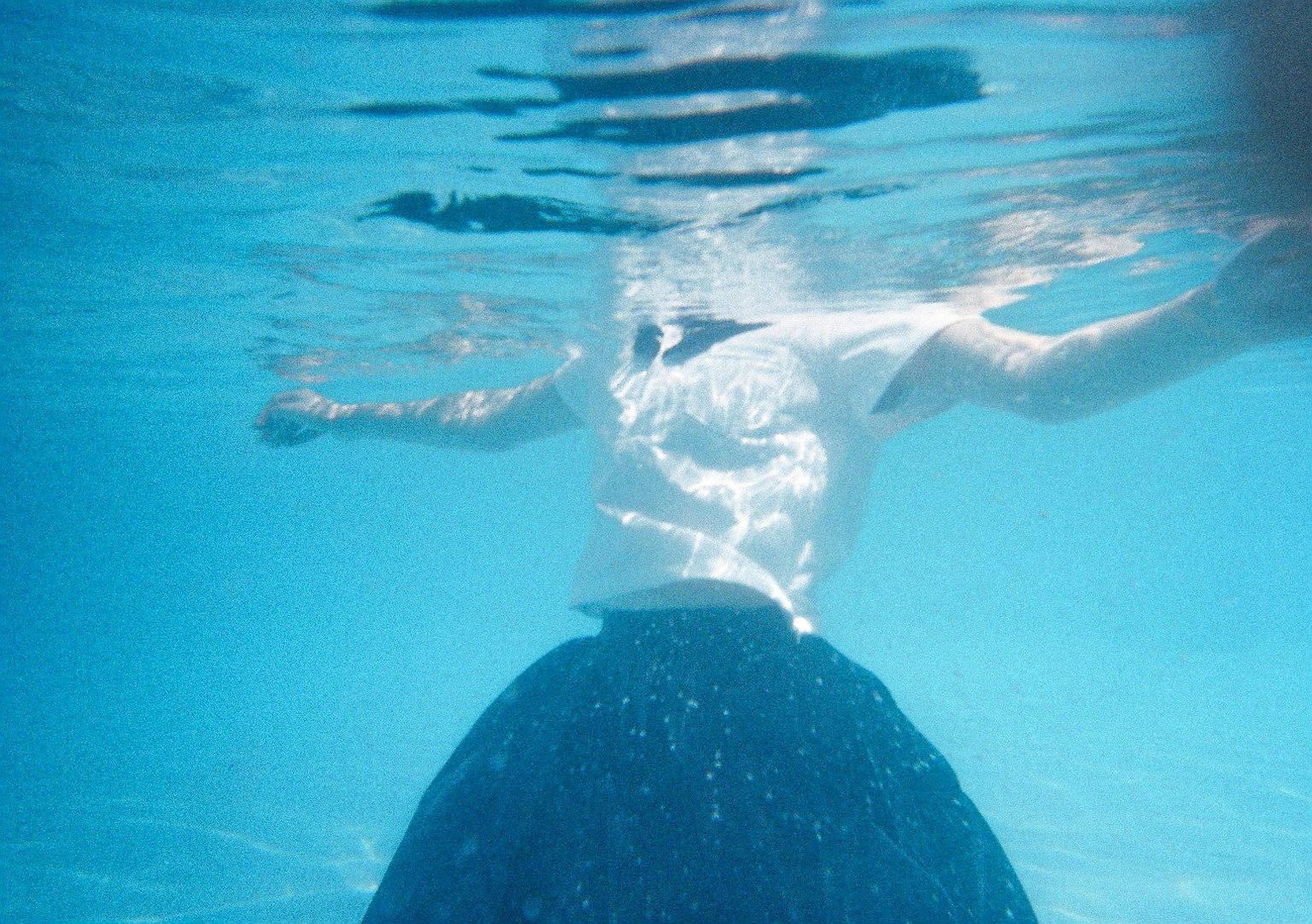 Person, die unter Wasser mit einem blauen Rock und einem weißen Oberteil schwebt
