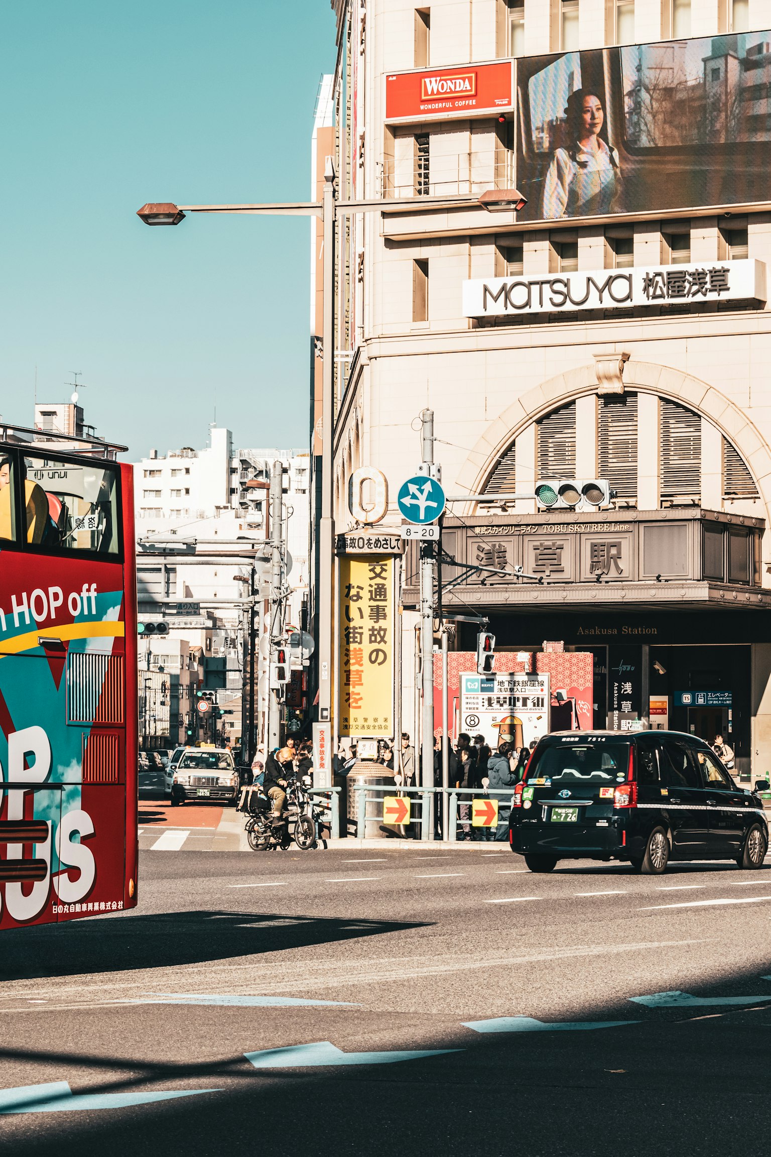 Esquina de calle concurrida con un autobús turístico rojo y un taxi en movimiento