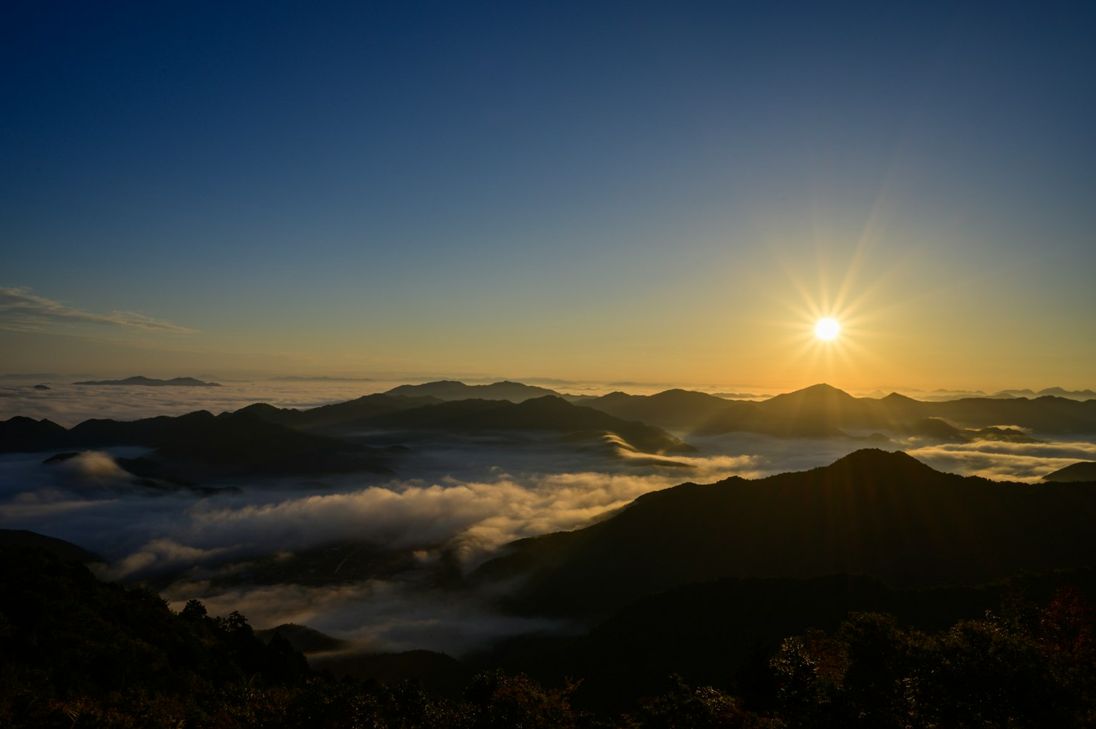美丽的日出在山脉上方，雾气弥漫的山谷和晴朗的蓝天