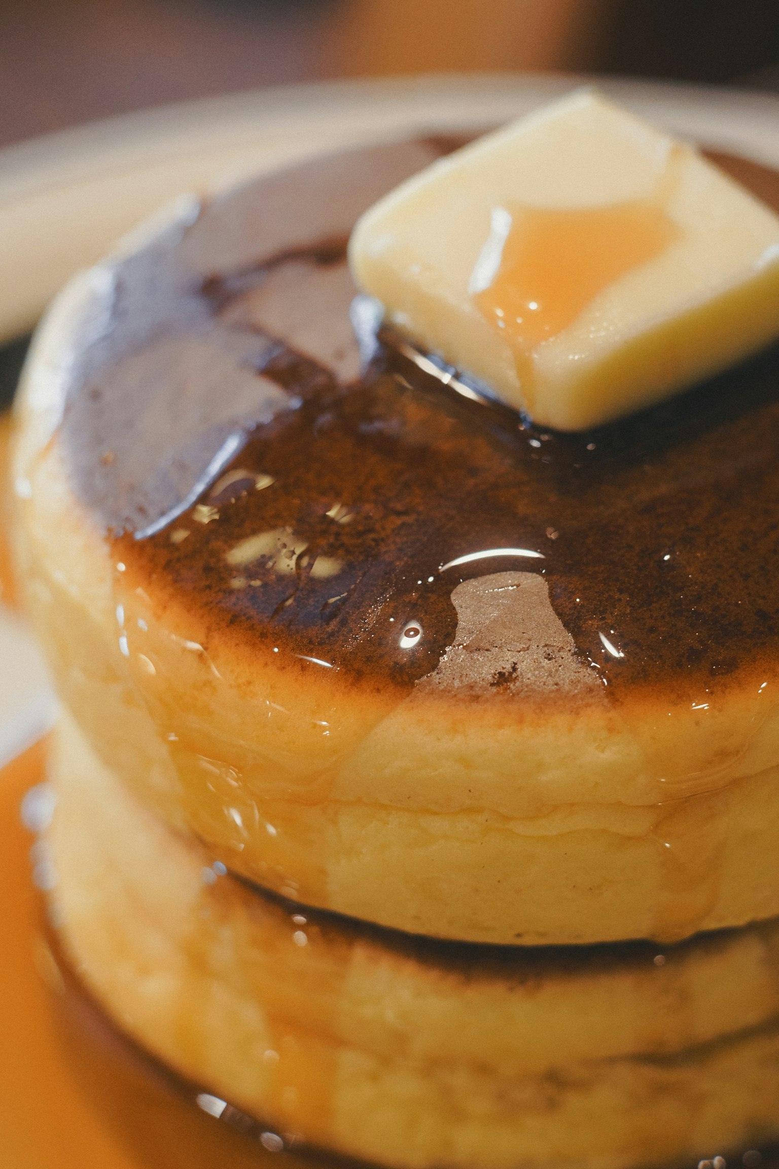 三枚のふわふわのパンケーキにバターとメープルシロップがかかっている