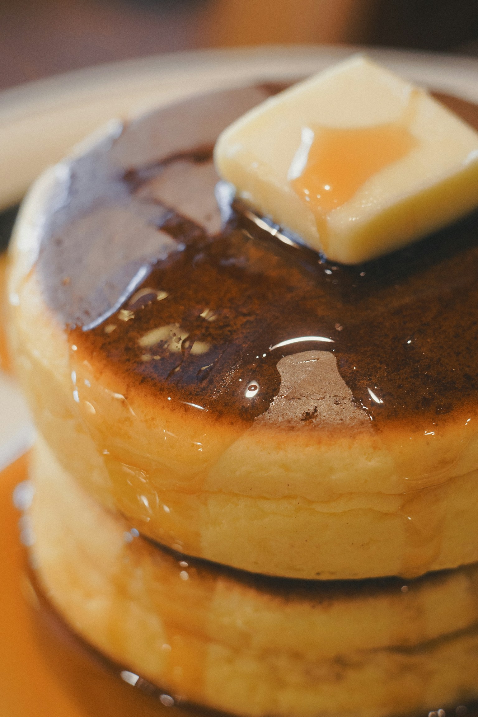 三枚のふわふわのパンケーキにバターとメープルシロップがかかっている