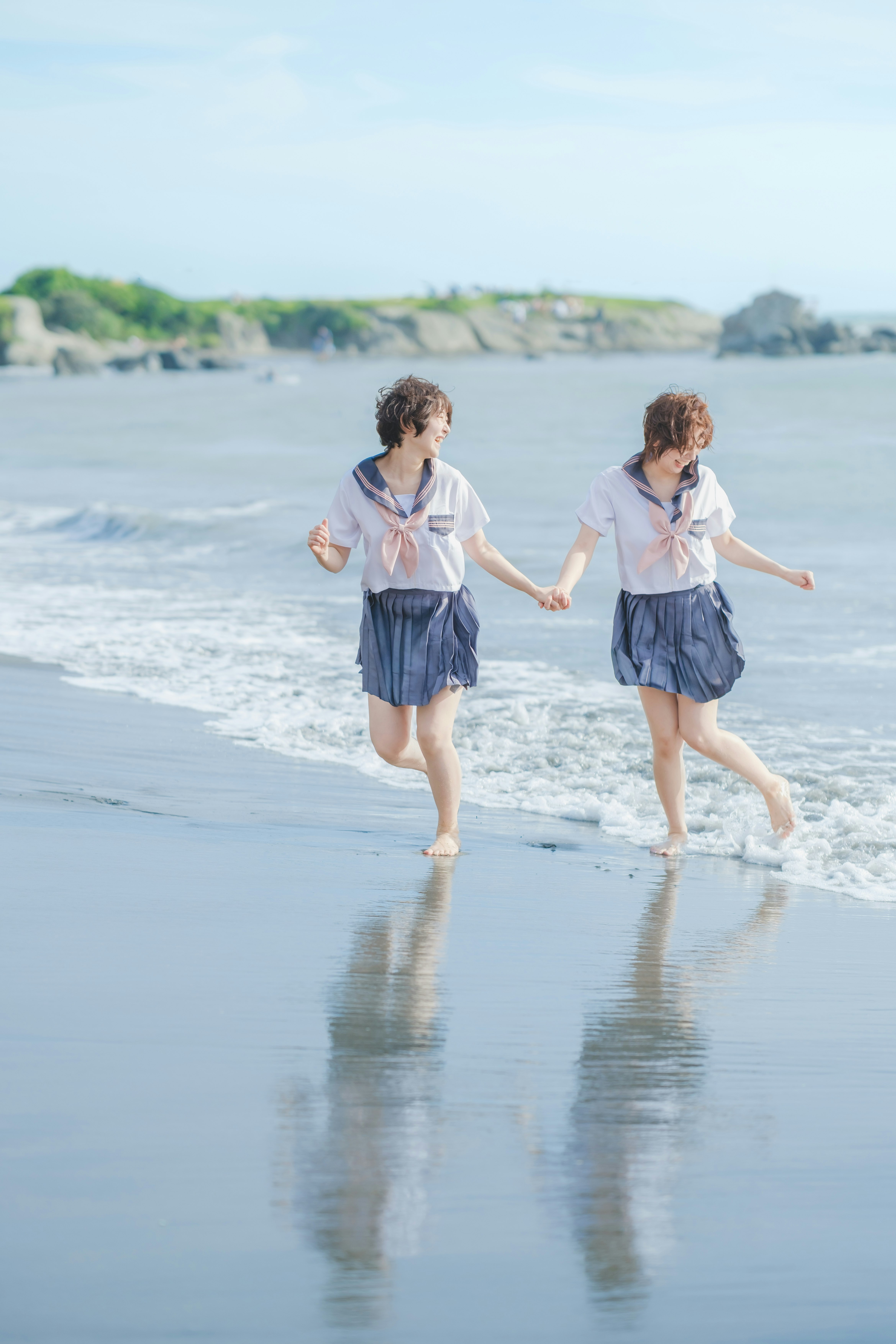 葉山の海岸でセーラー服を着た2人が波打ち際を歩く