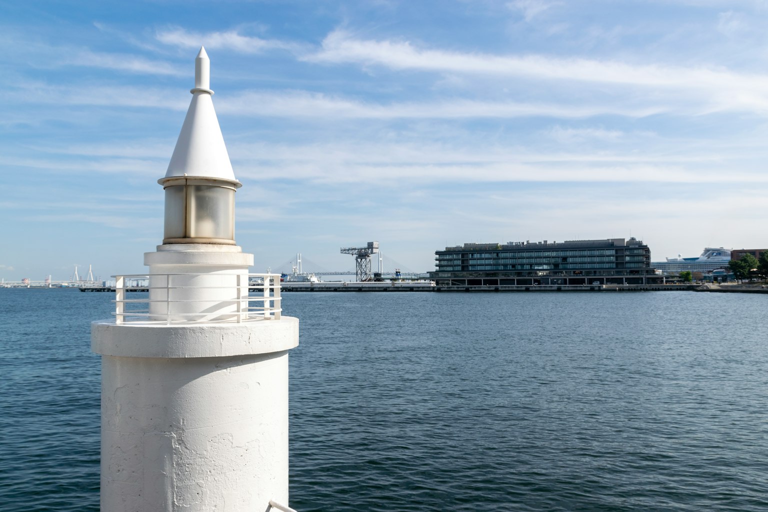 Faro blanco con mar tranquilo y edificios a lo lejos