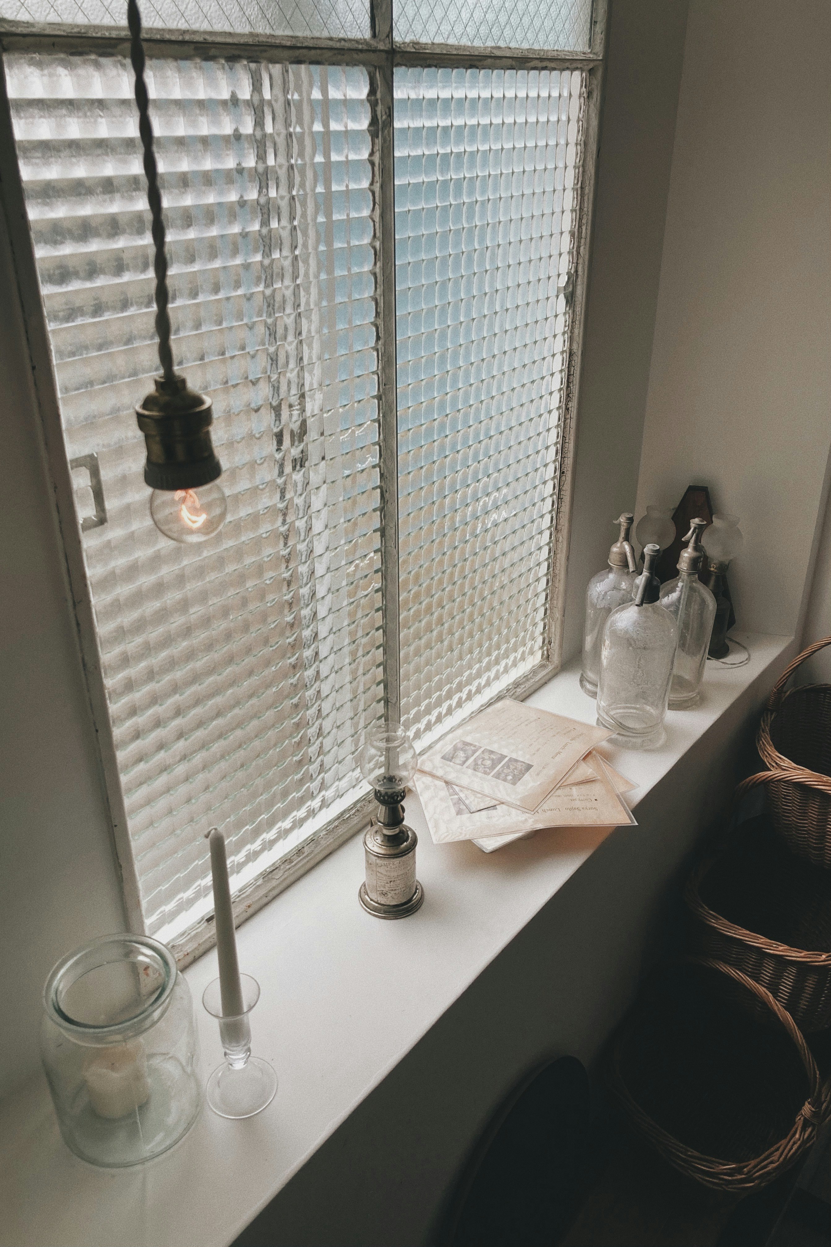 ruhige Ecke im Innenraum mit weißen Jalousien, Kerzen und Glasdeko am Fenster