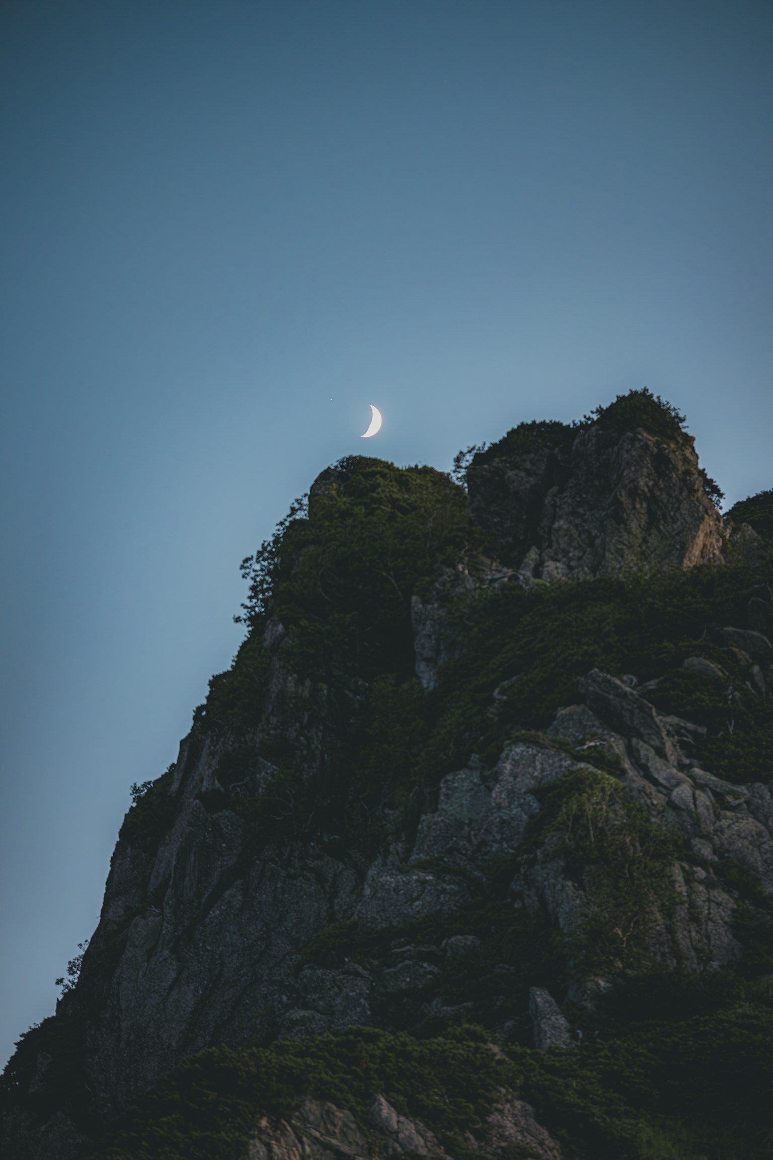 Cima di montagna con una luna crescente nel cielo blu