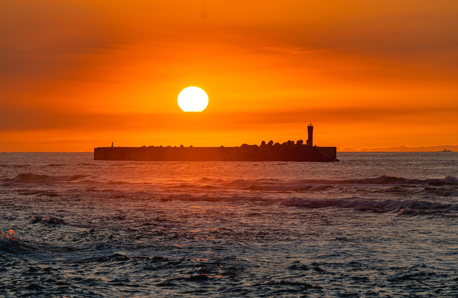Silhouette eines Wellenbrechers bei Sonnenuntergang über dem Ozean