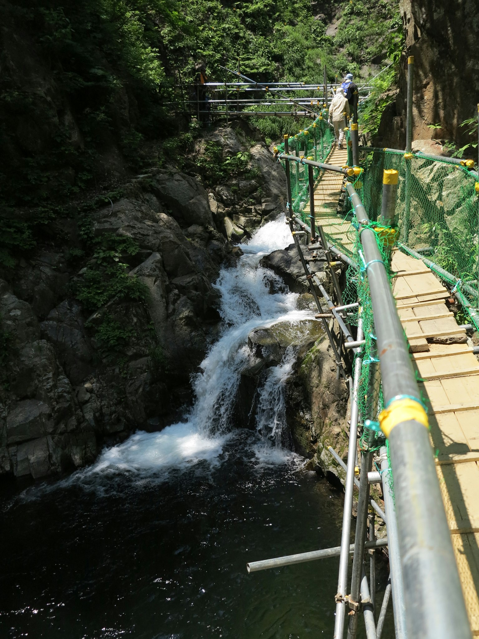 Ein malerischer Weg entlang eines Flusses mit einem Wasserfall, umgeben von Grün