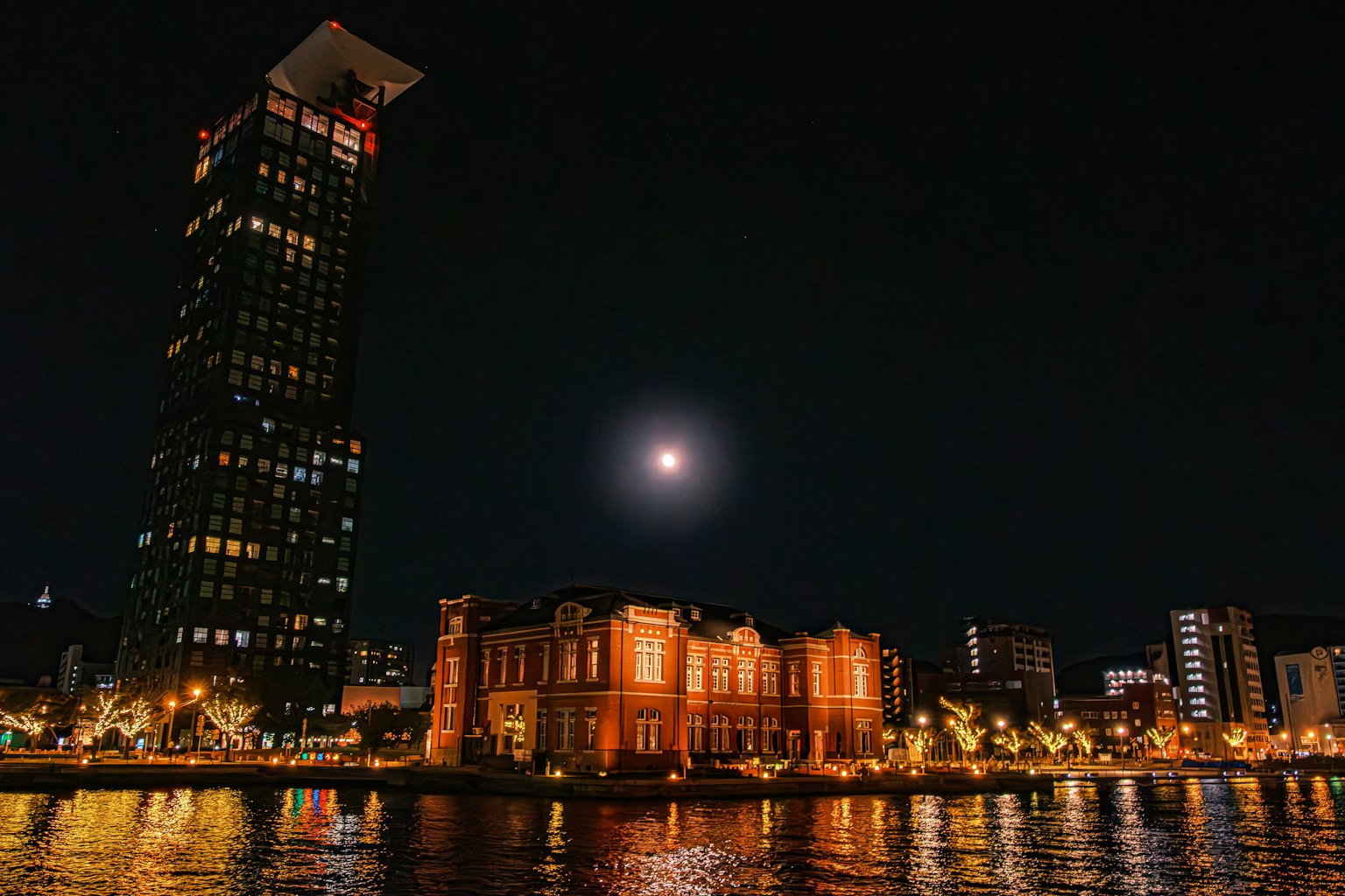 Vue nocturne d'un bord de rivière avec un bâtiment moderne et une structure historique illuminée