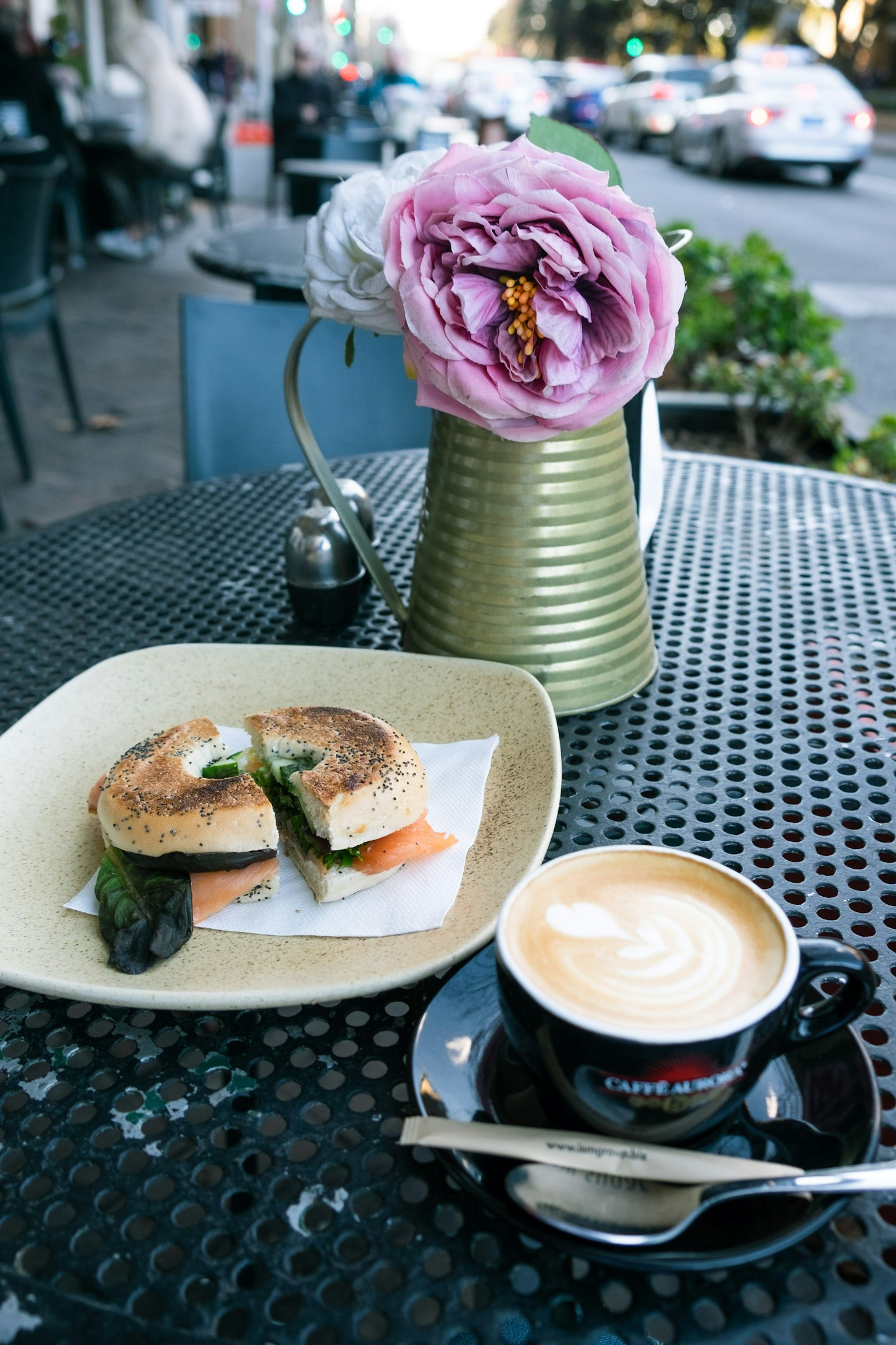 Un piatto con un panino e una tazza di caffè su un tavolo con un vaso di fiori contenente peonia
